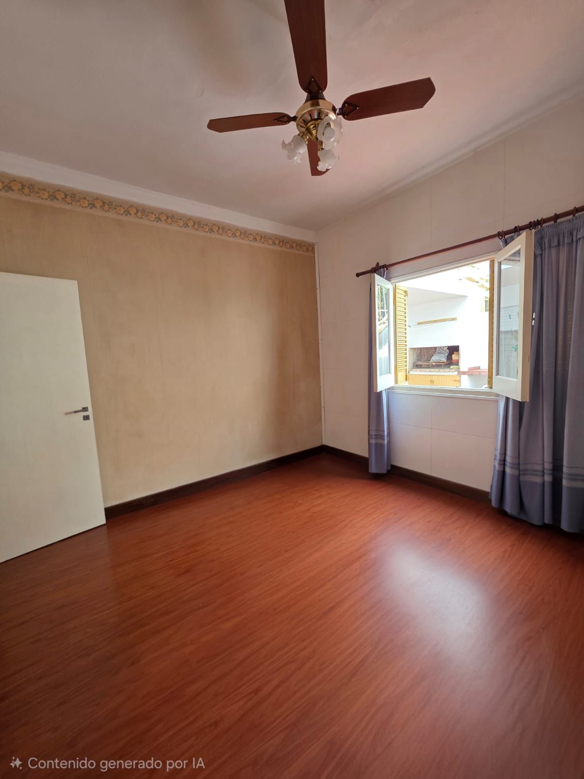 Habitación vacía de color beige con suelo de madera, ventilador de techo y ventana abierta con cortinas azules.