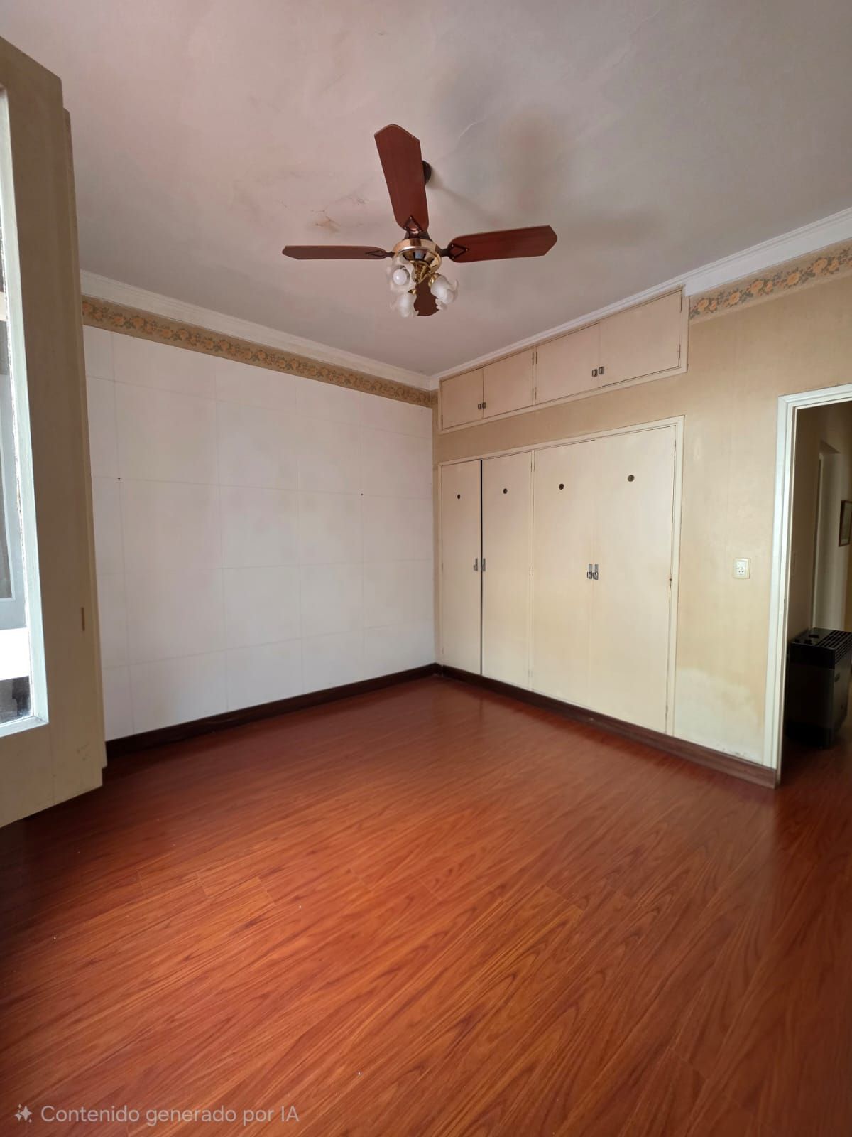 Habitación vacía con suelo de madera rojiza, paredes beige, ventilador de techo y armarios empotrados.