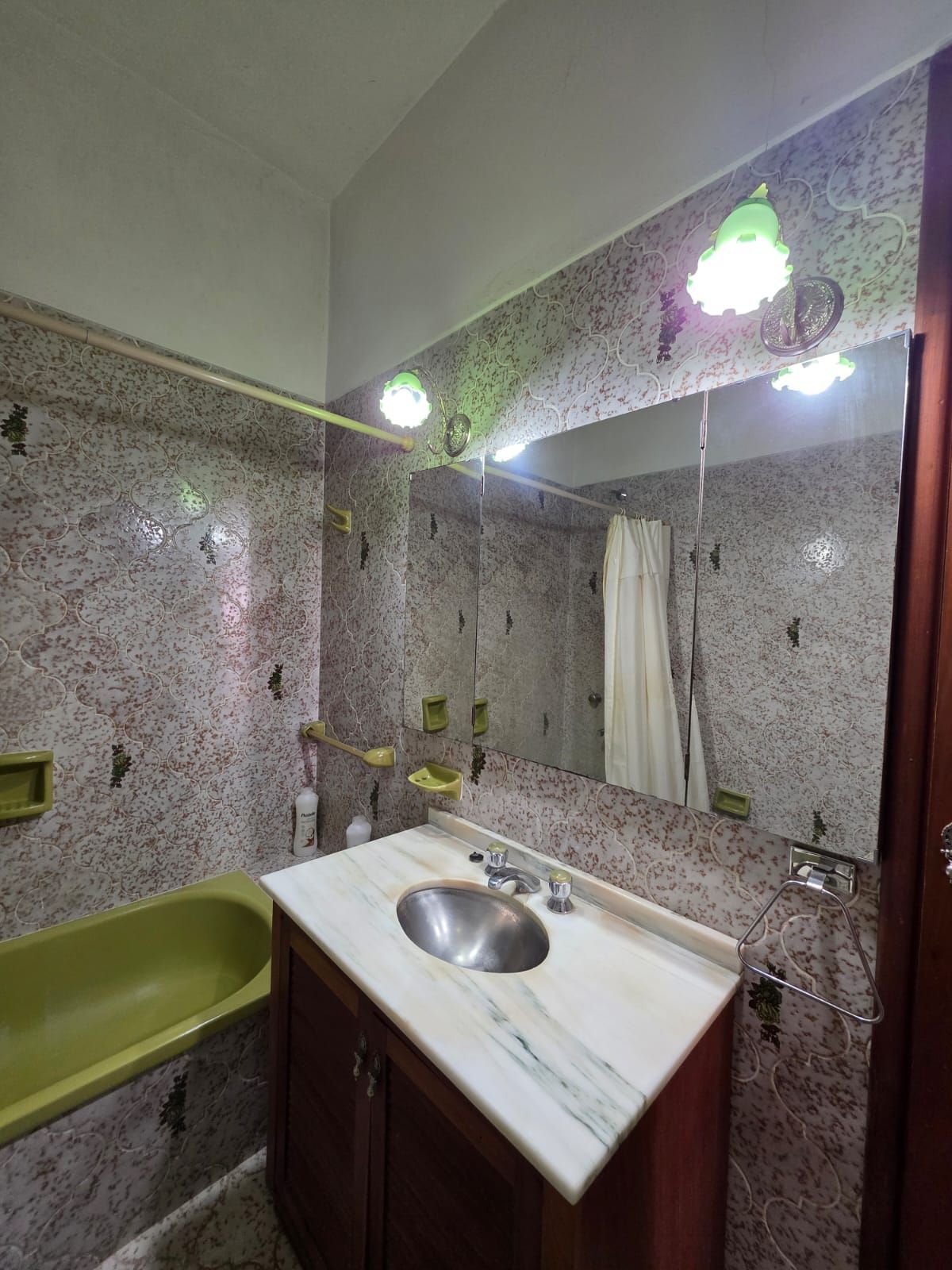 Baño pequeño con azulejos, bañera verde, lavabo blanco, espejo y apliques de pared.
