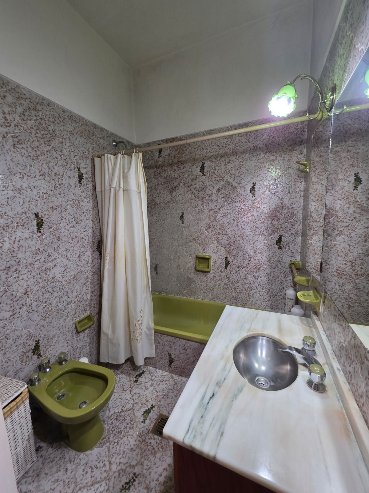 Baño pequeño con azulejos, inodoro verde, bañera, lavabo y cortina blanca.