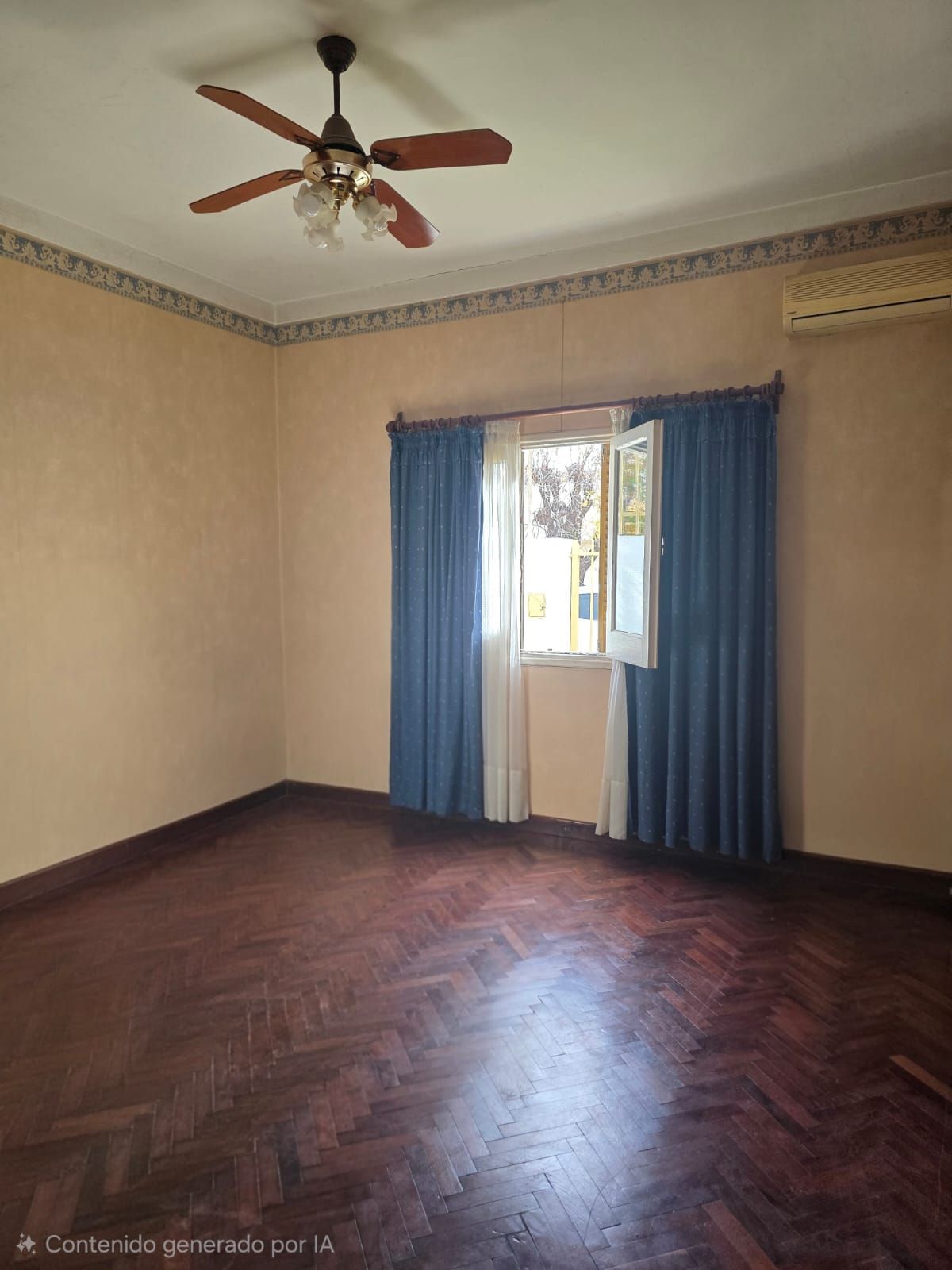 Habitación vacía con paredes beige, suelo de madera oscura, cortinas azules y un ventilador de techo cerca de una ventana.