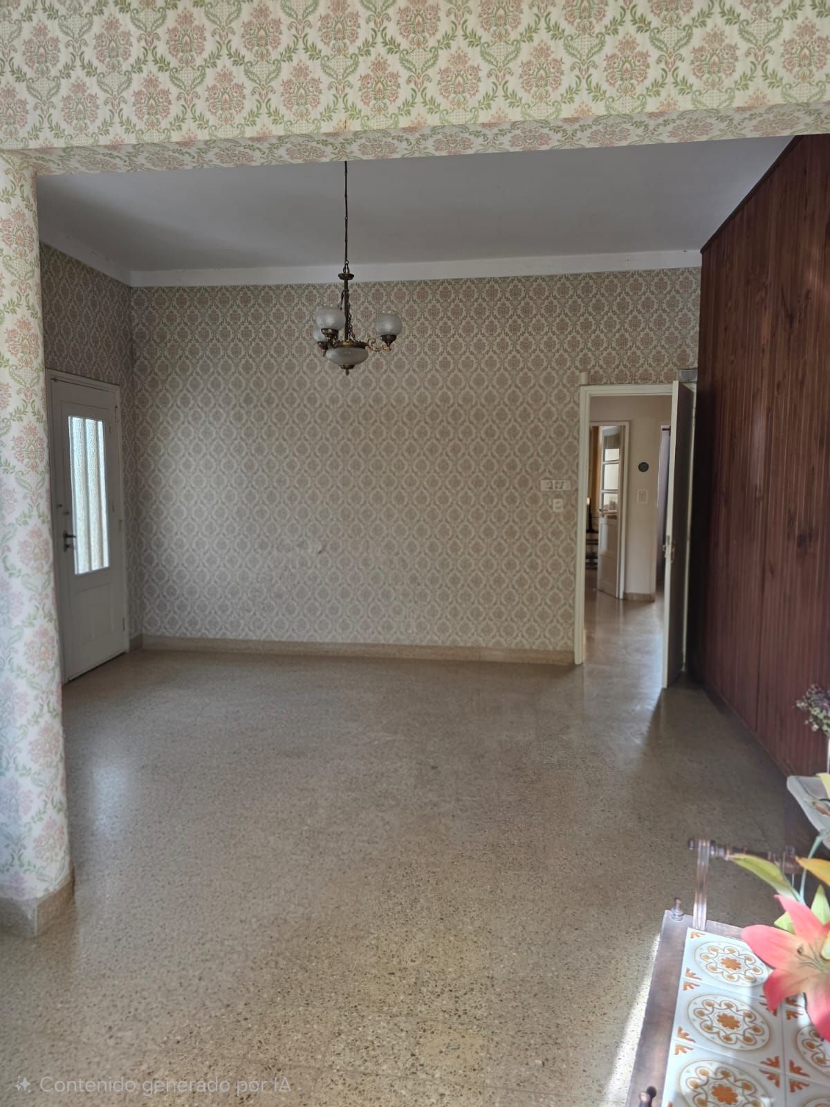 Sala de estar vacía de estilo vintage con papel tapiz estampado, lámpara de araña y piso de baldosas, vista desde la puerta.