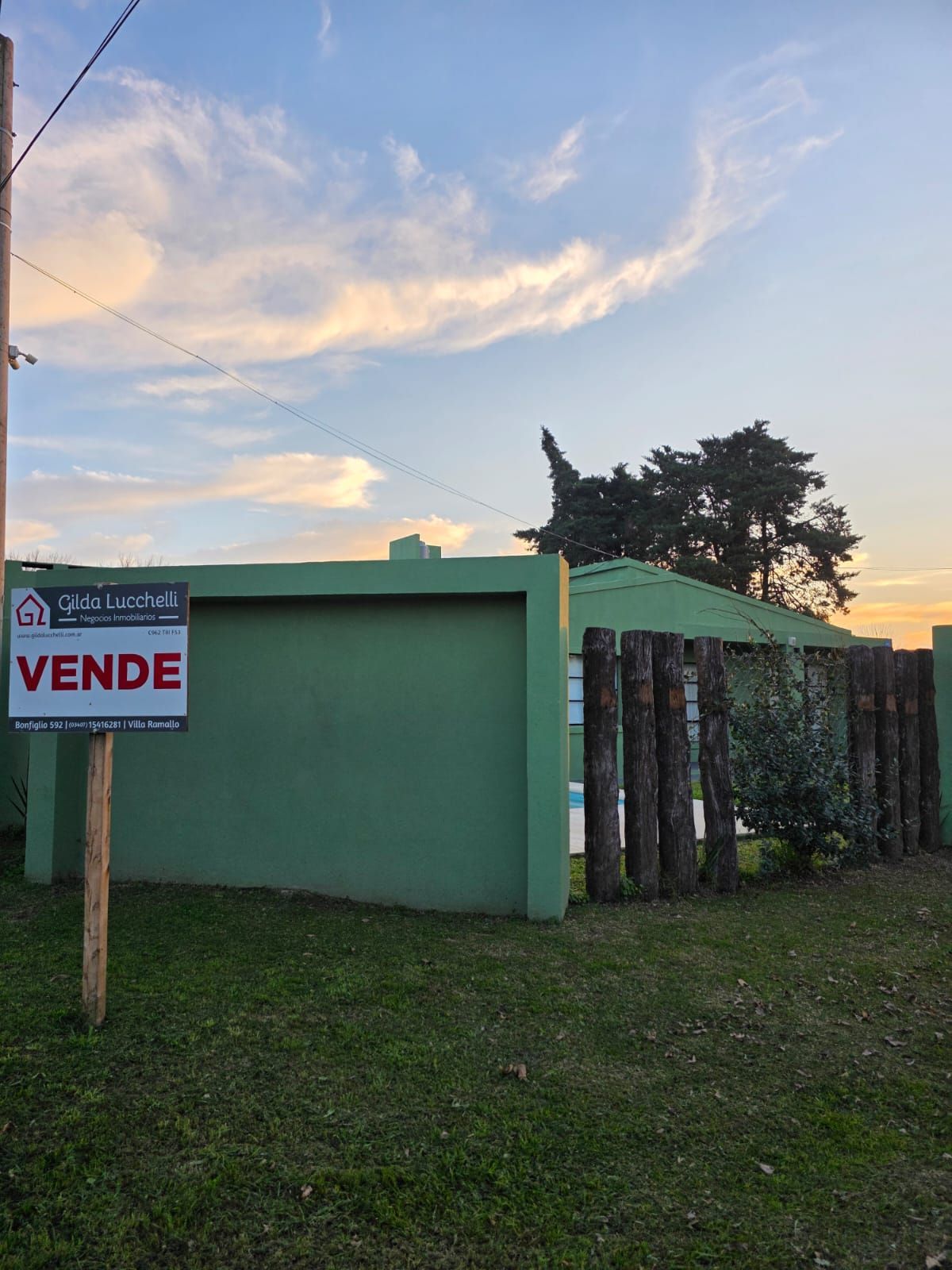 Un cartel verde indica que se vende una casa pequeña de color verde menta al atardecer.