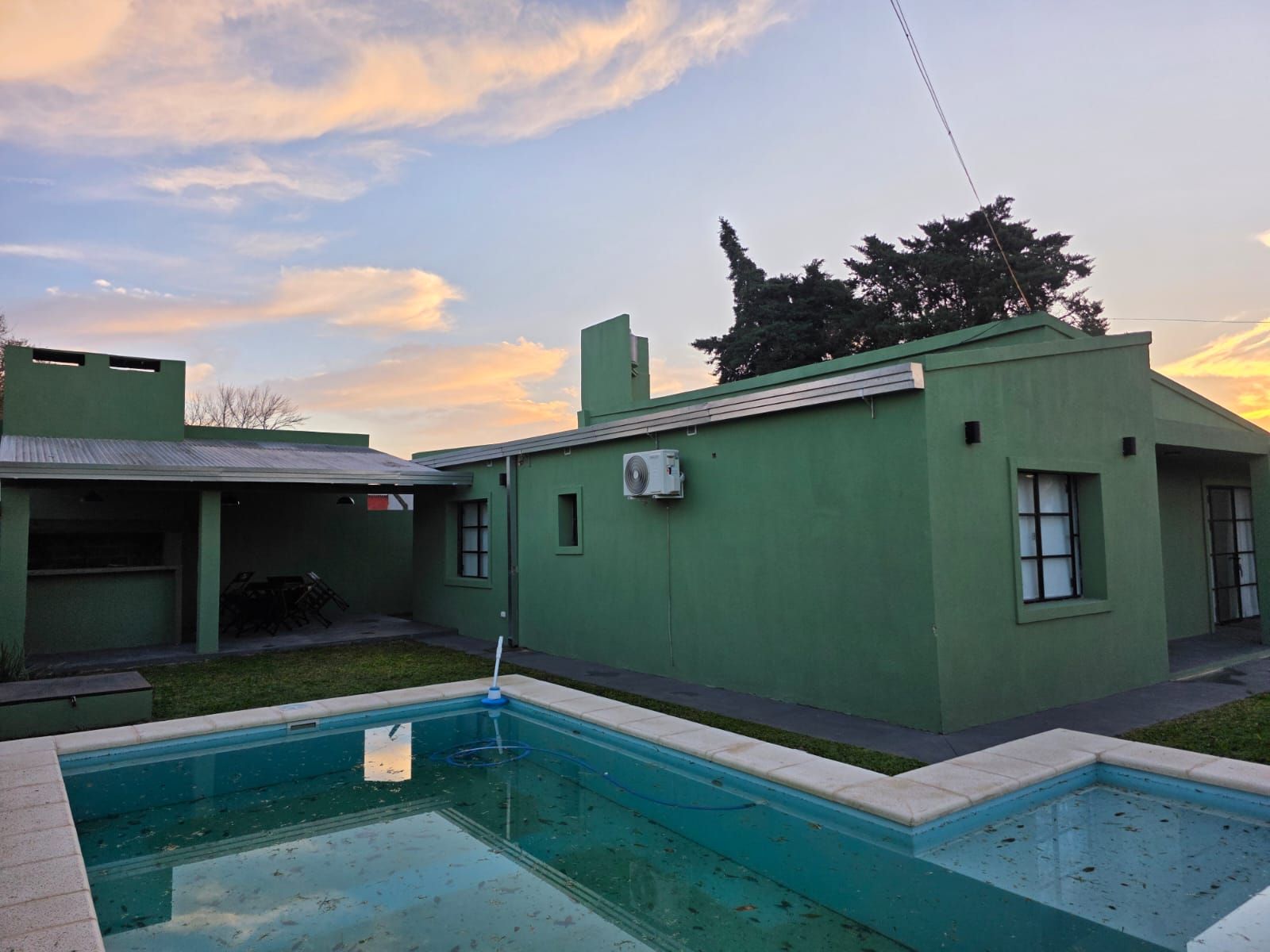 Casa con patio verde y piscina al atardecer.