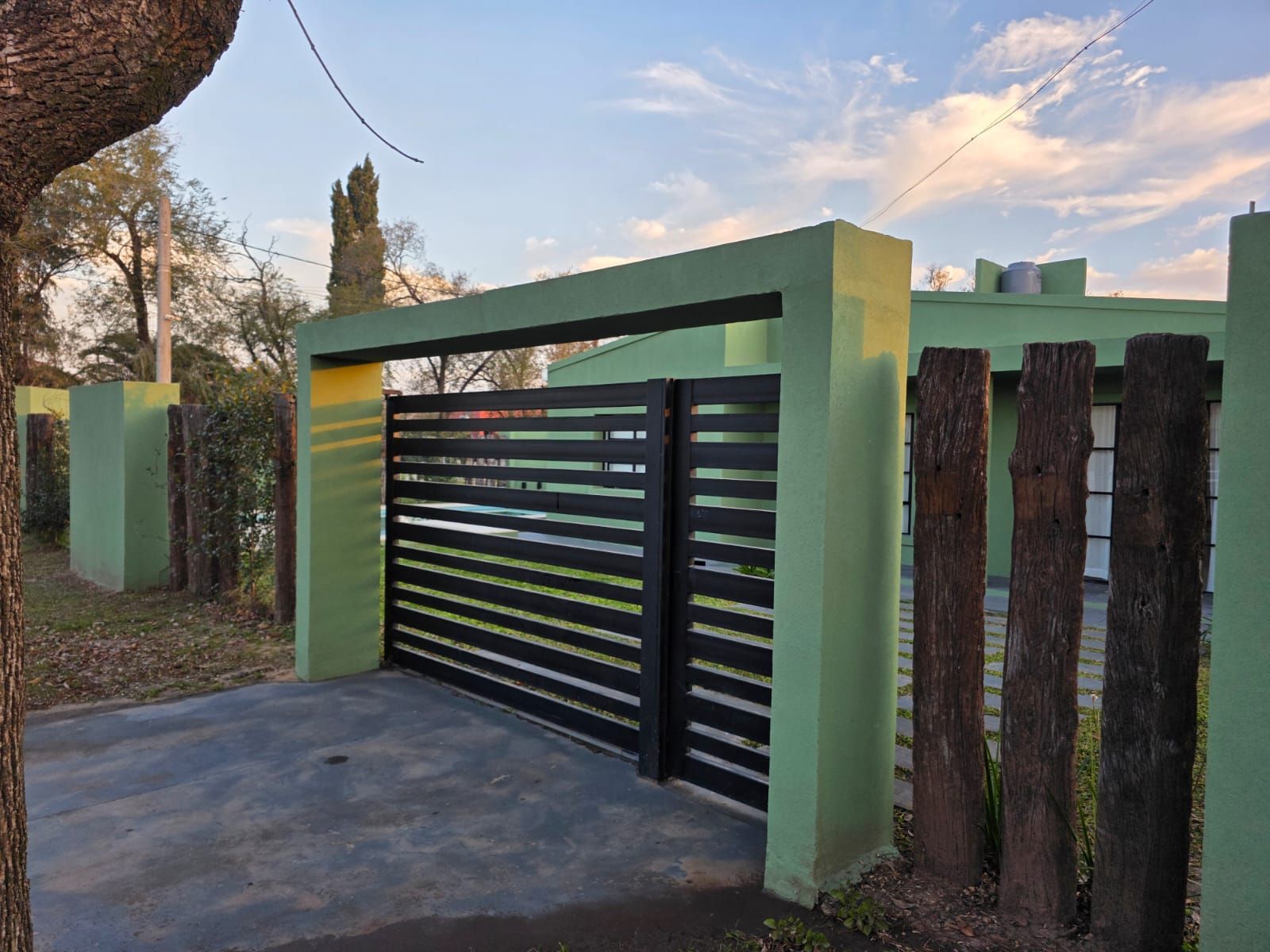 Portón de entrada verde con puerta de metal con listones negros