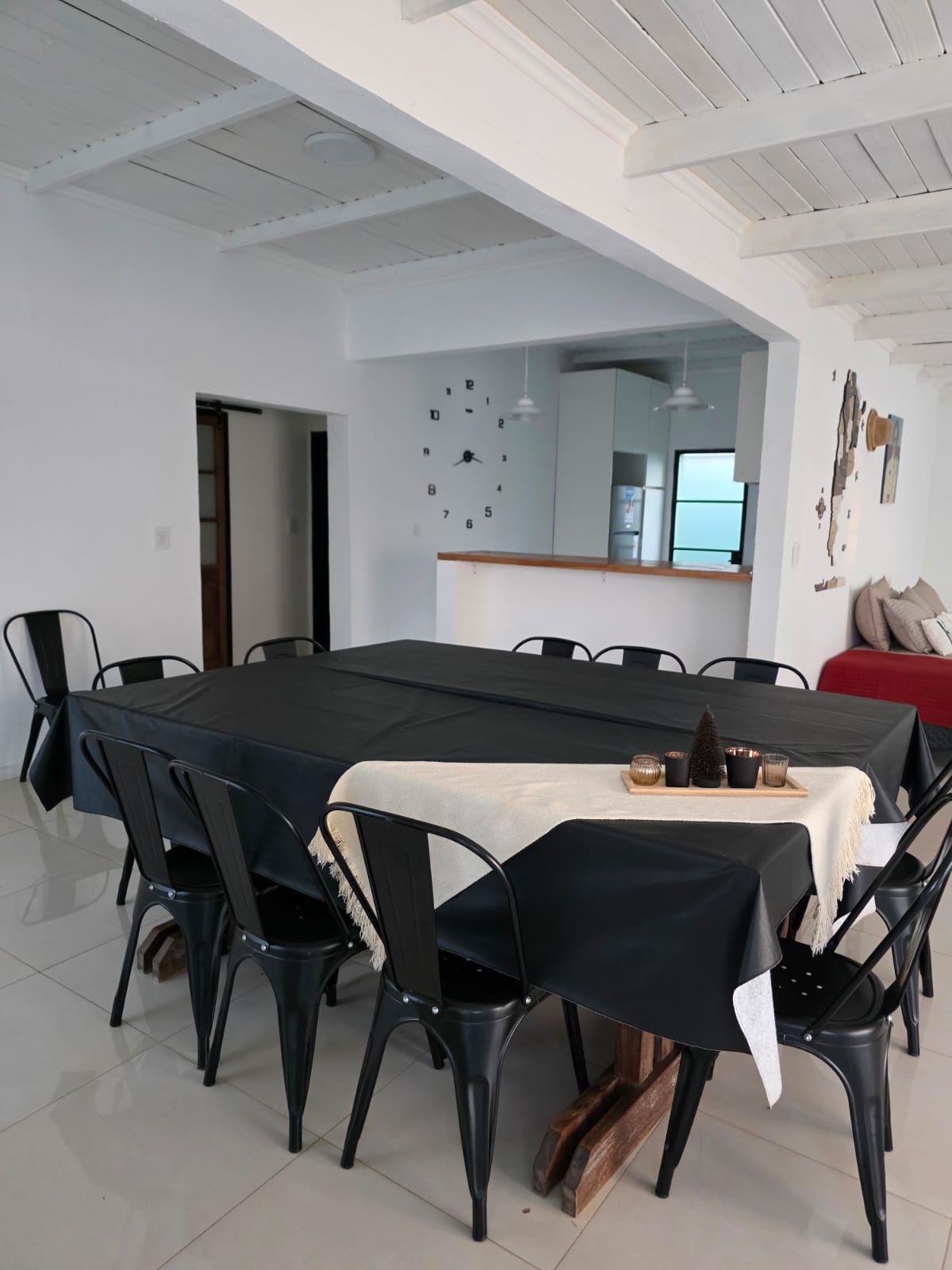 Comedor con mesa y sillas negras, mantel beige y techo con vigas blancas a la vista.