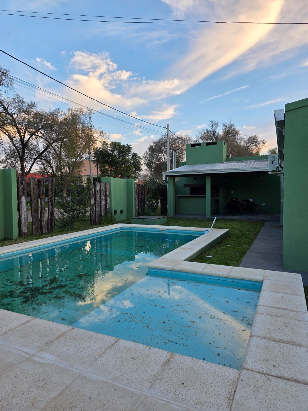 Patio trasero con piscina y jacuzzi junto a un invernadero al atardecer.