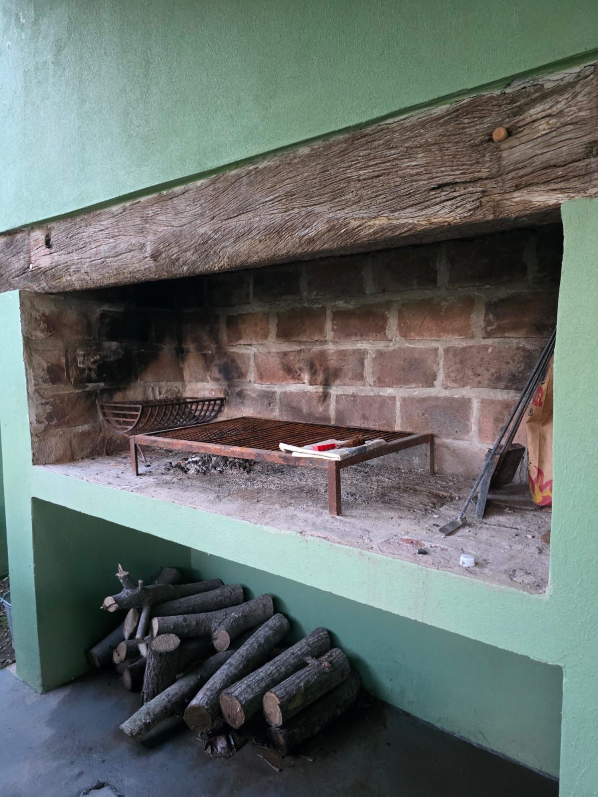 Chimenea de piedra con repisa de madera rústica, pared trasera de ladrillo y troncos apilados debajo.