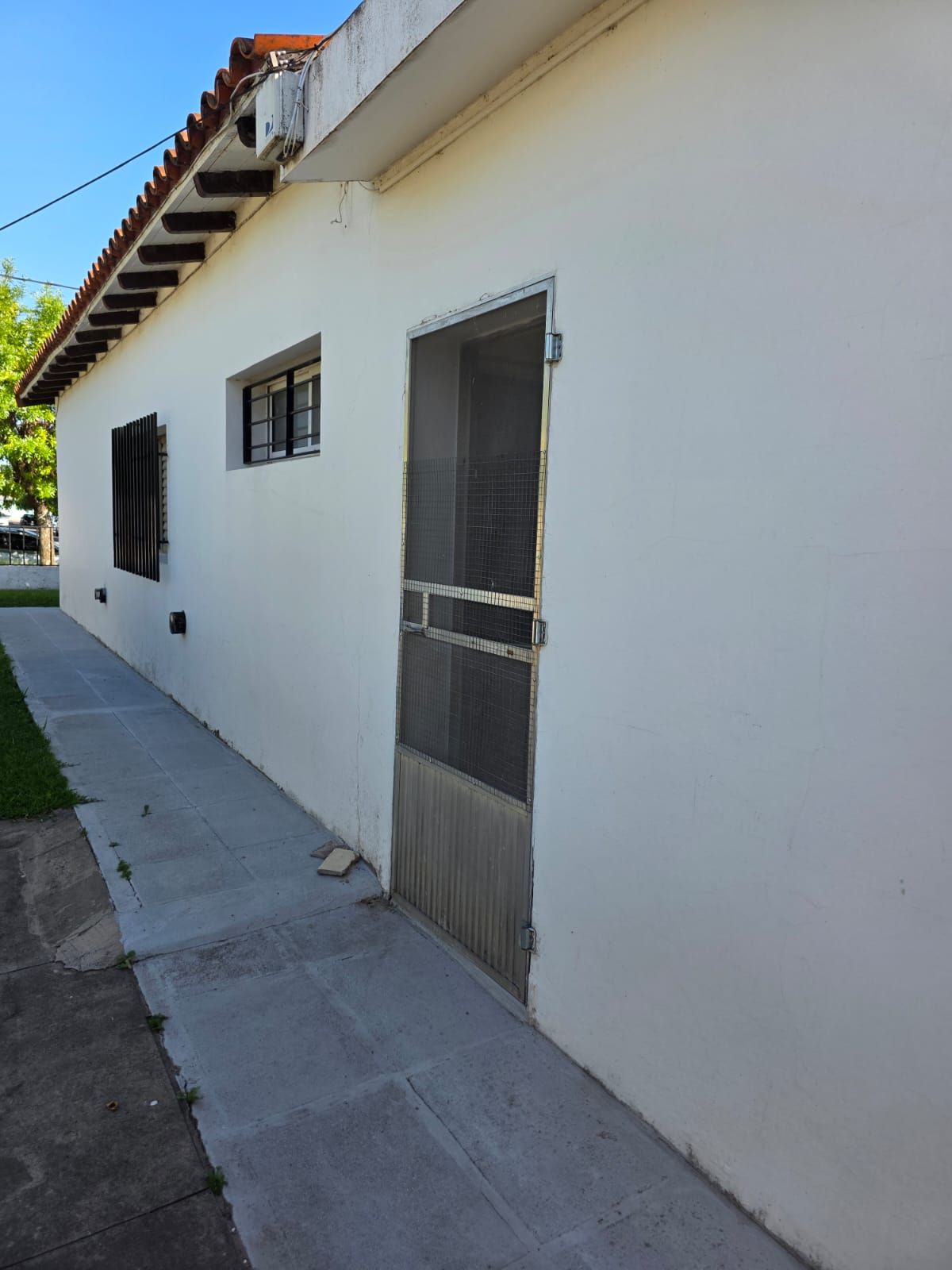 Exterior de una casa de estuco blanco con ventanas y una puerta a lo largo de un estrecho sendero de hormigón.