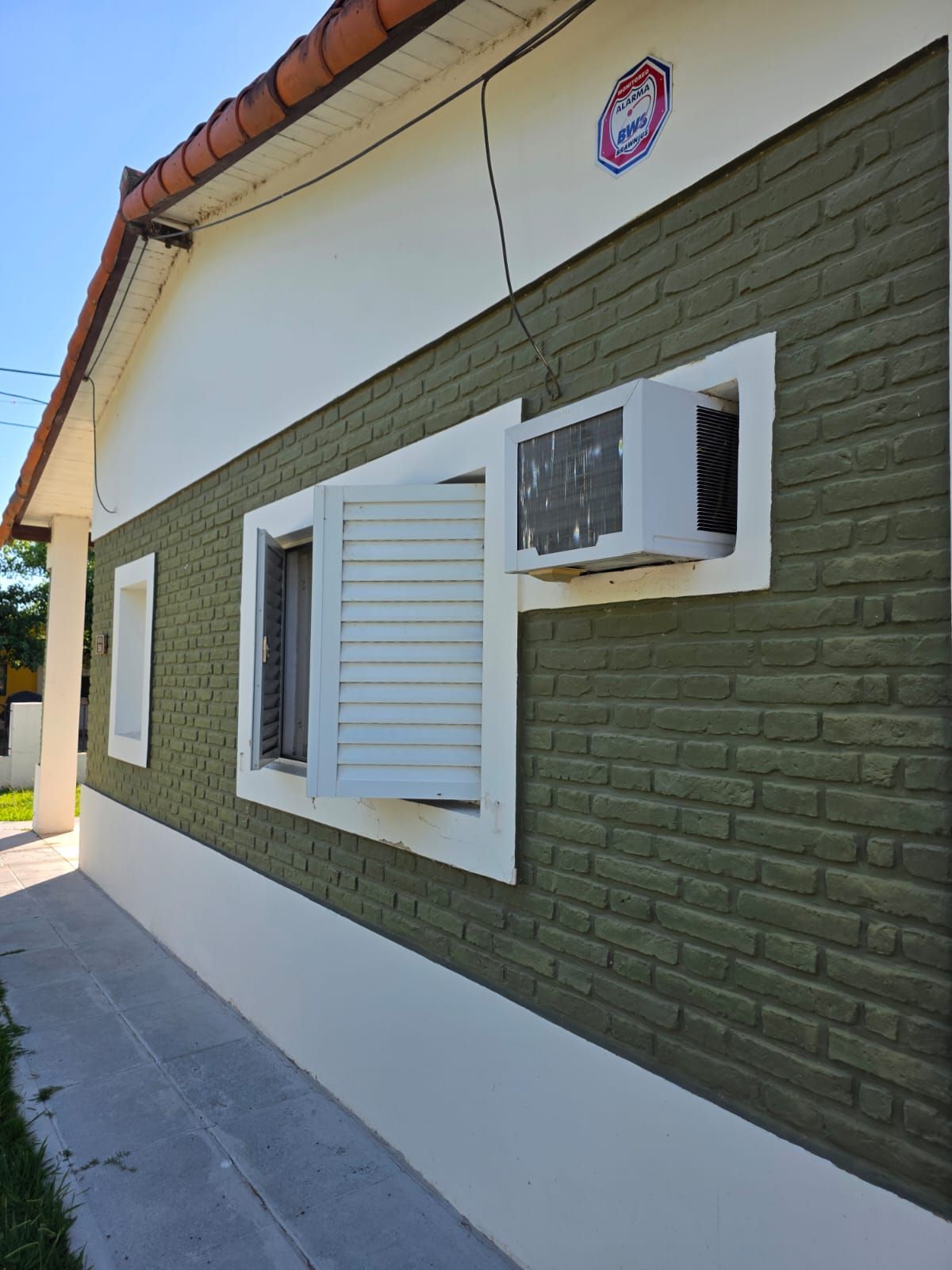 Pared exterior de una casa con revestimiento verde, molduras blancas, contraventanas abiertas y borde de teja.