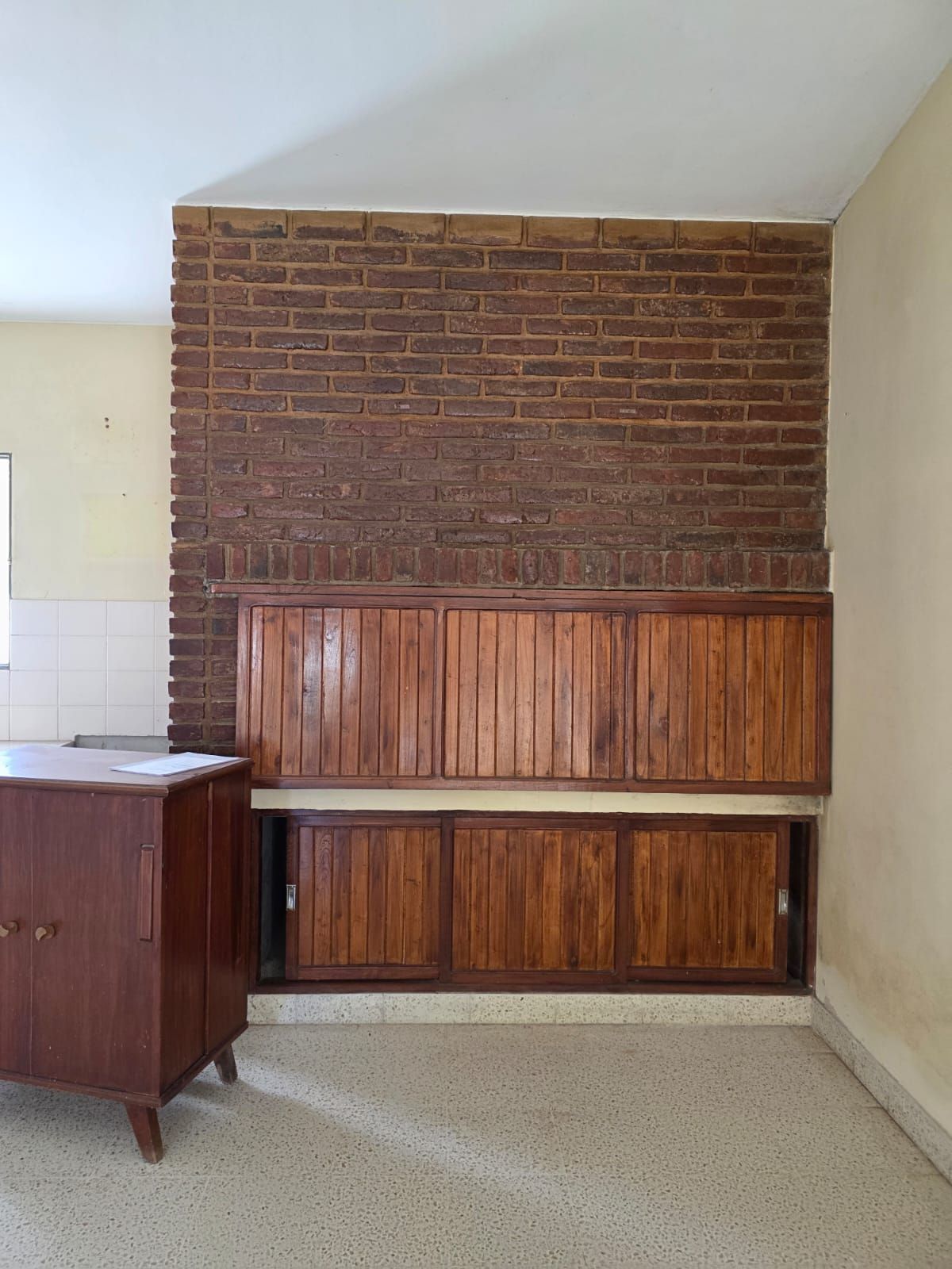 Habitación pequeña con una pared de chimenea de ladrillo, revestimiento de madera y un armario lateral a la izquierda.