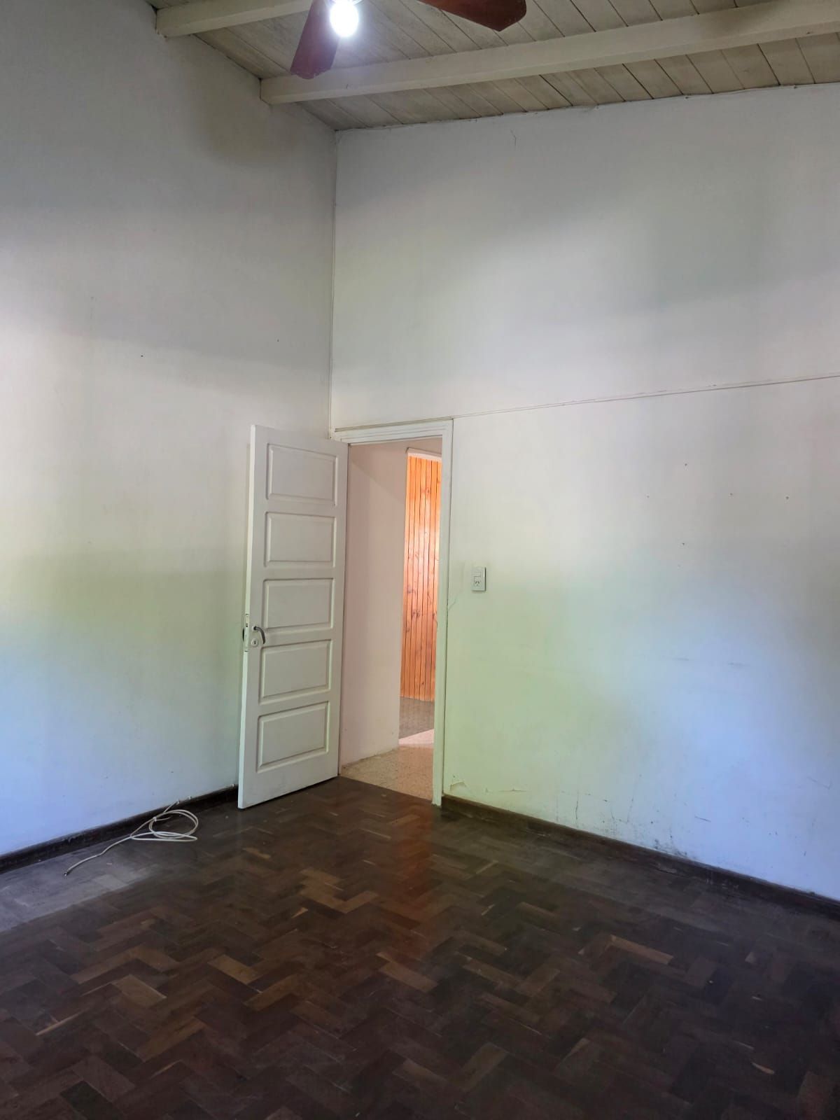 Habitación blanca vacía con la puerta abierta, suelo de madera oscura y luz de color suave en las paredes.