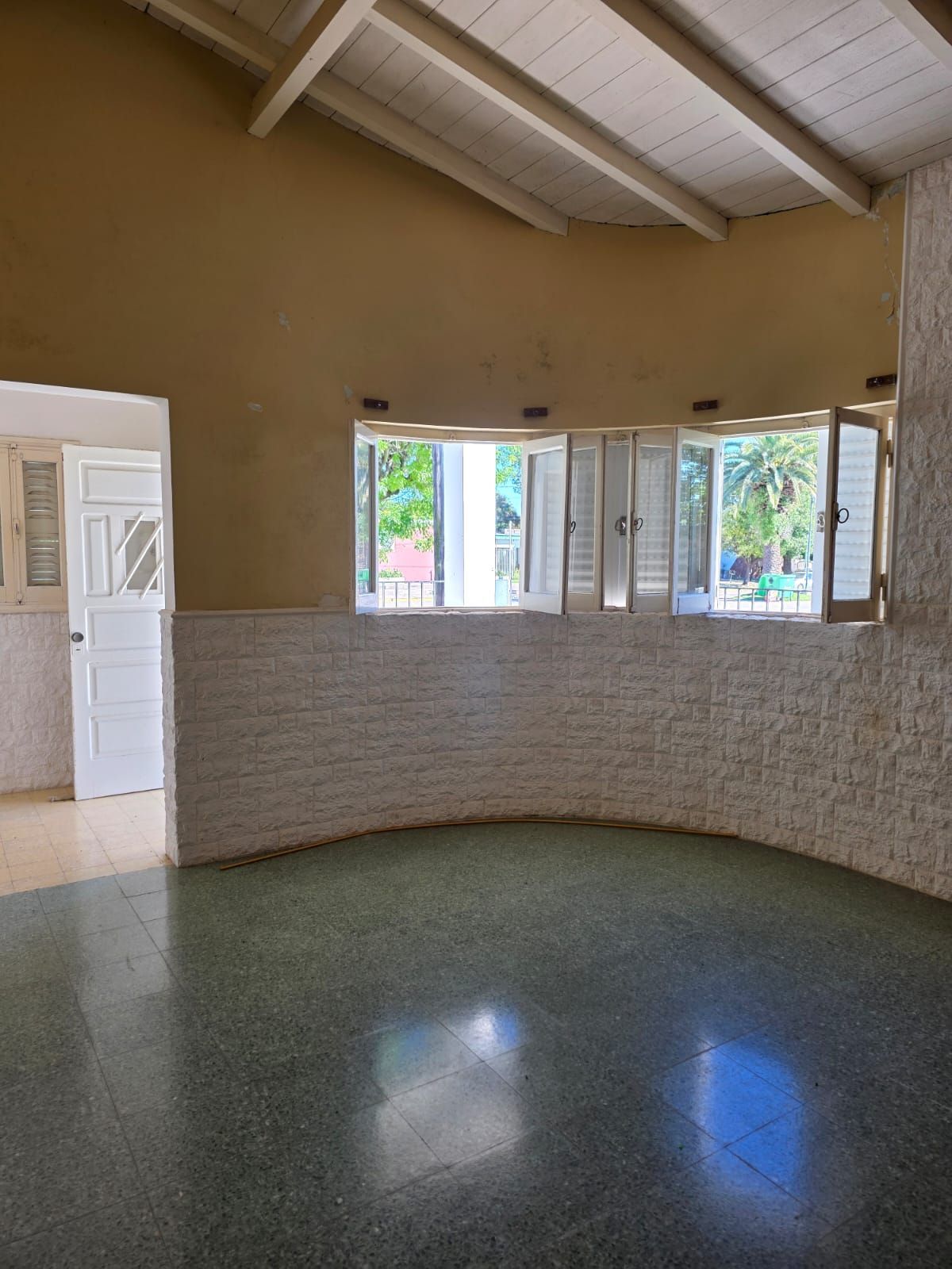 Habitación vacía con azulejos, ventanas arqueadas, contraventanas blancas y techo alto con vigas a la vista.
