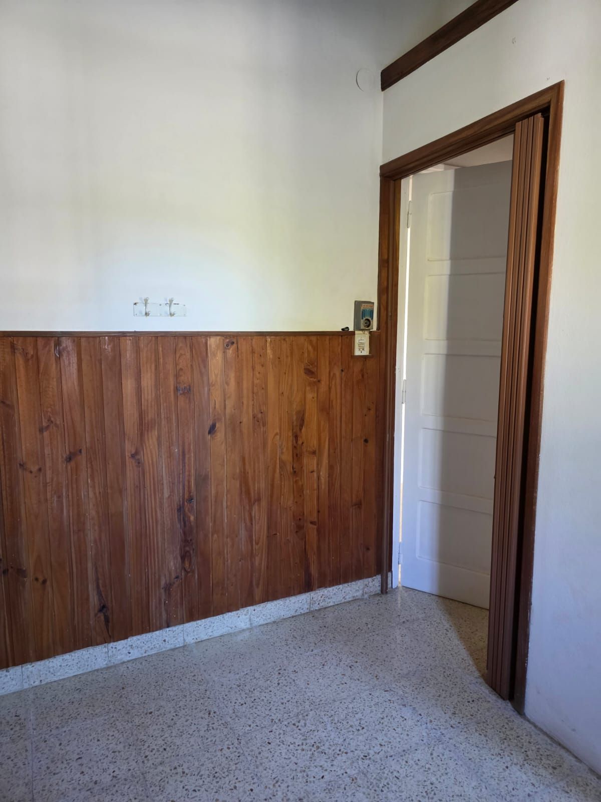 Habitación pequeña con paredes inferiores revestidas de madera, paredes superiores blancas y una puerta abierta.