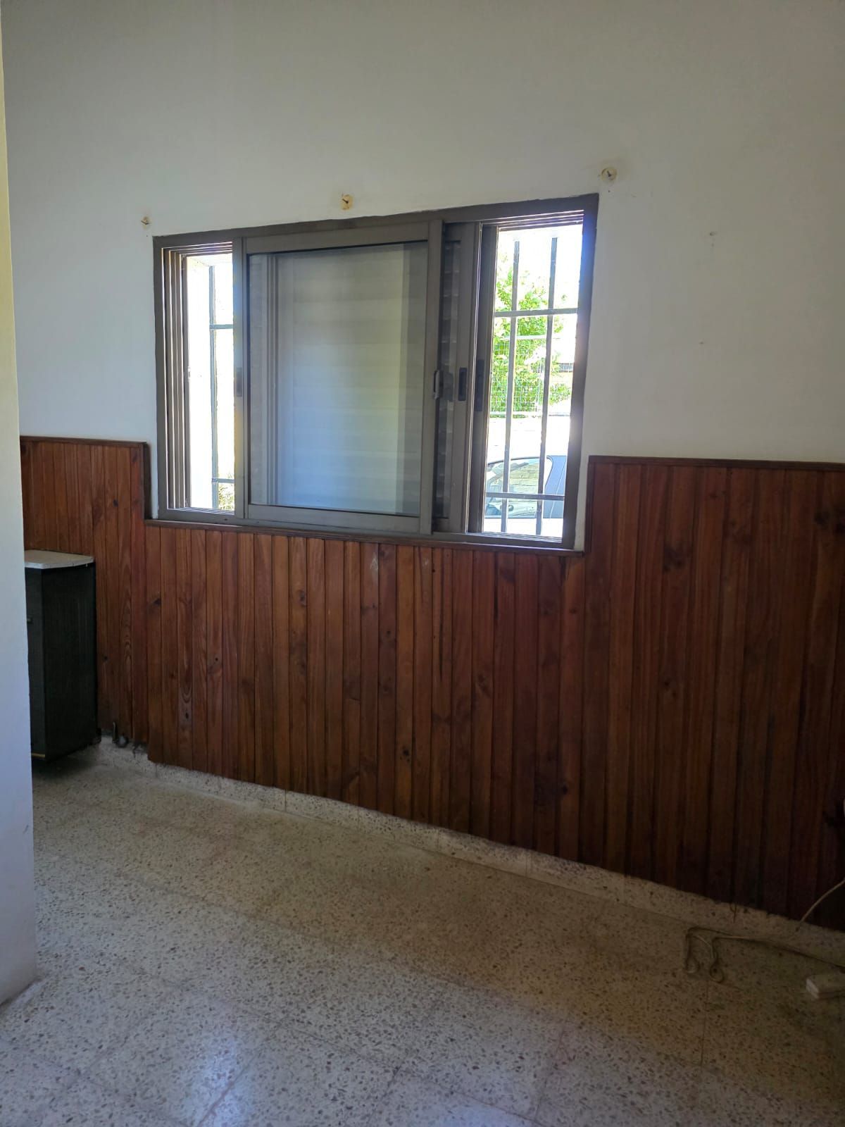 Habitación vacía con paredes inferiores revestidas de madera, suelo moteado y una ventana abierta.