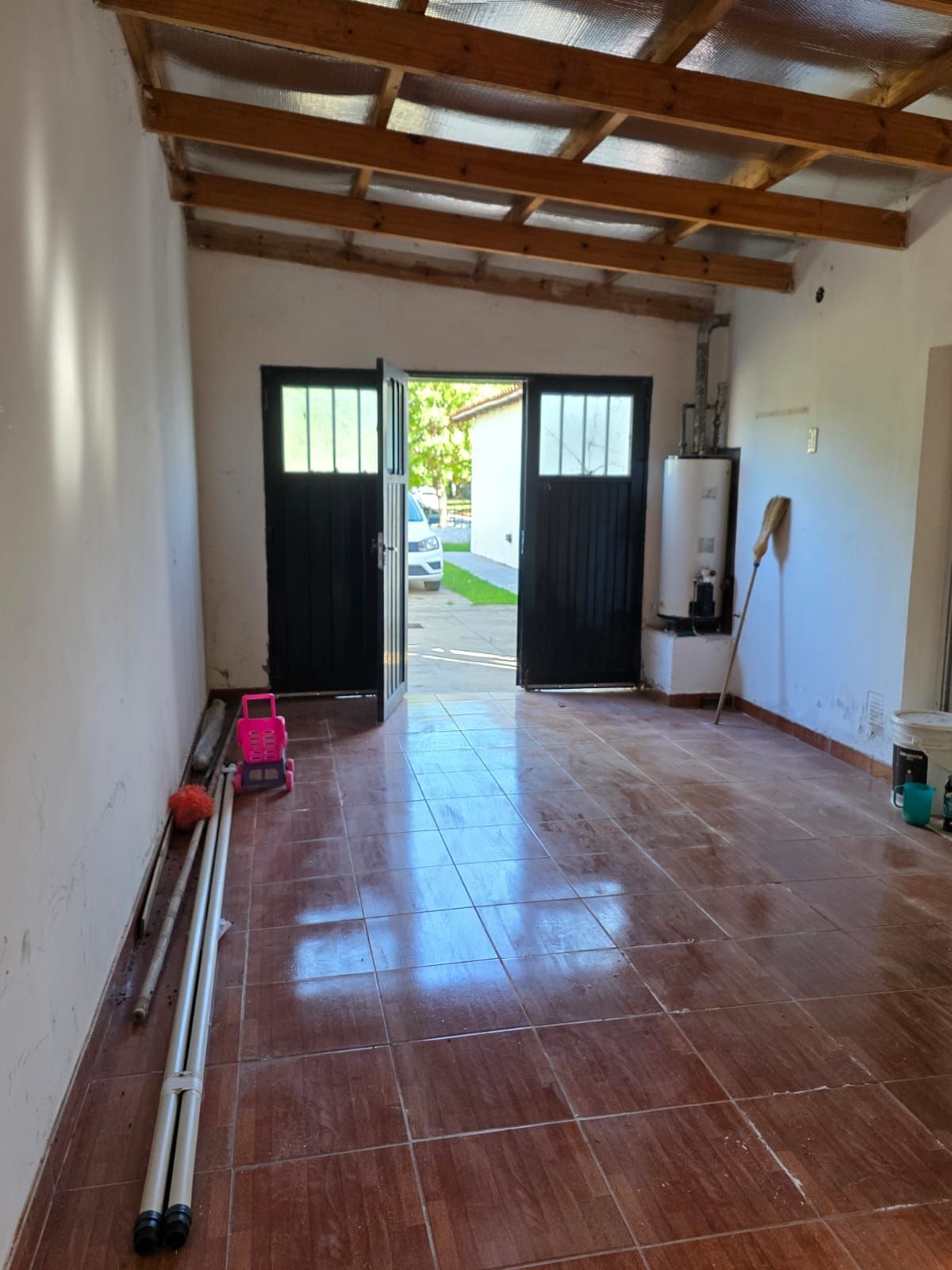 Habitación vacía con suelo de baldosas, vigas de madera a la vista y puertas dobles abiertas que dan al exterior.