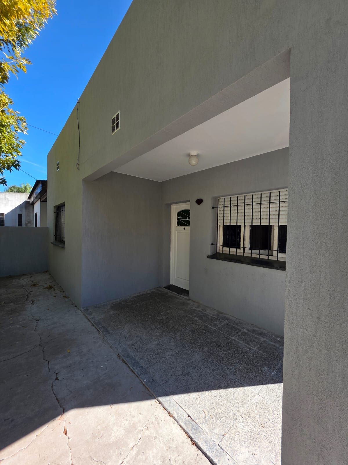 Entrada a una casa de color gris con porche cubierto, puerta blanca y ventana con barrotes