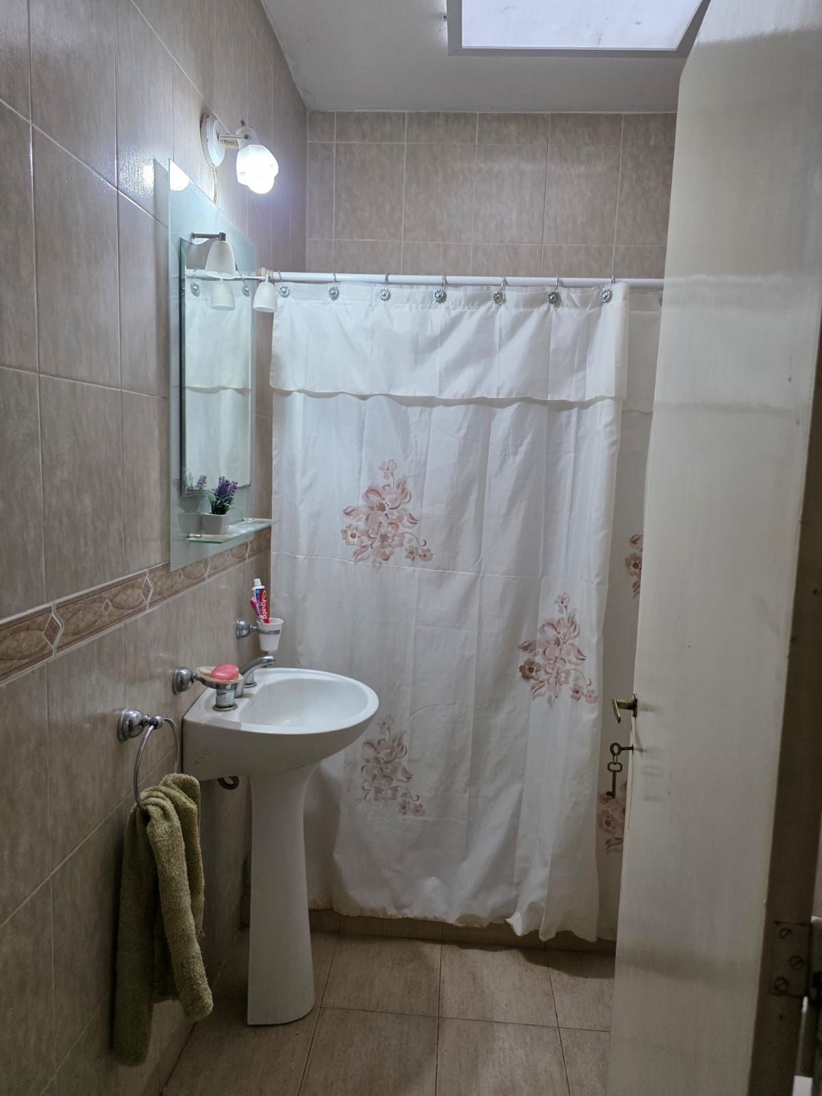 Baño pequeño con lavabo de pedestal, espejo, toalla y cortina de ducha blanca.