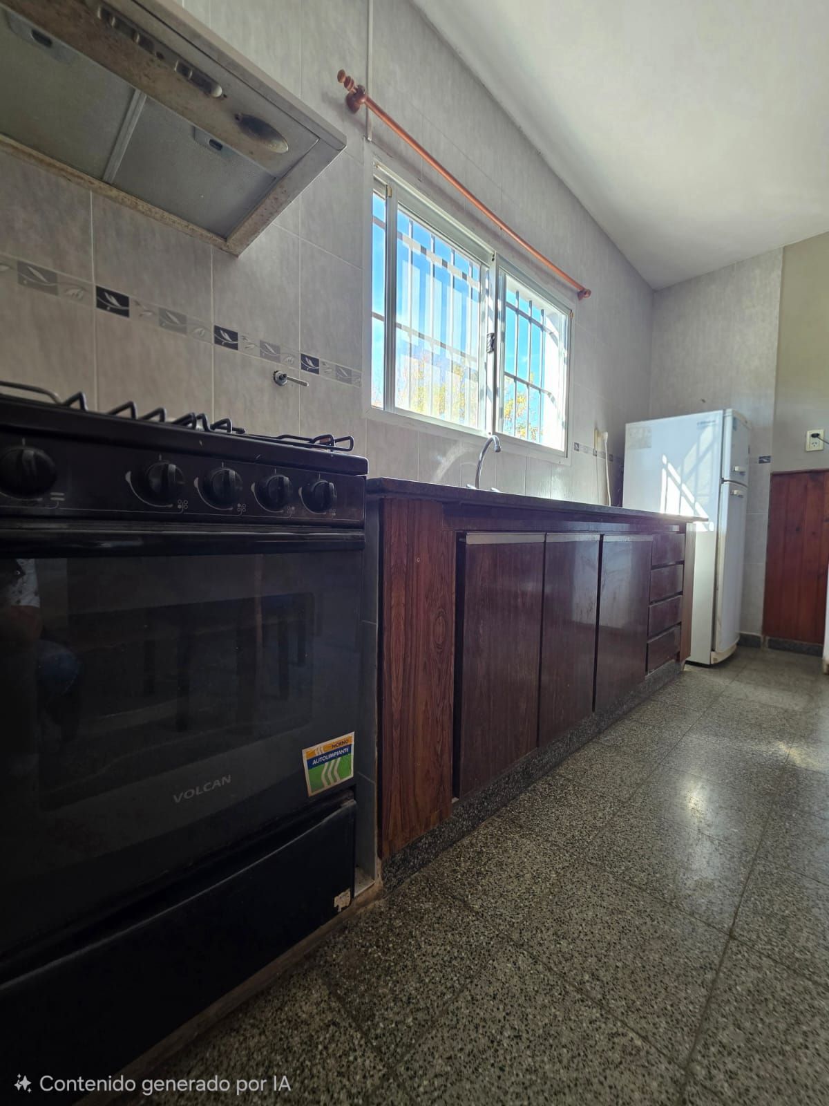 Cocina pequeña con estufa negra, armarios de madera, una ventana y suelo de baldosas moteadas.