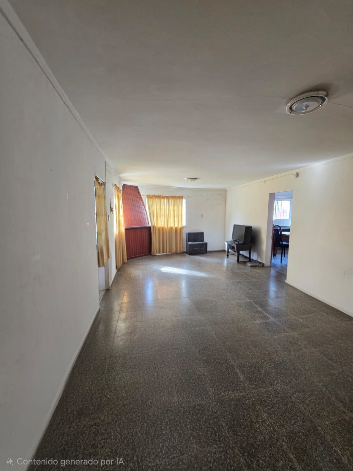 Sala de estar vacía con suelo de baldosas, paredes blancas, cortinas y un televisor cerca de la pared del fondo.