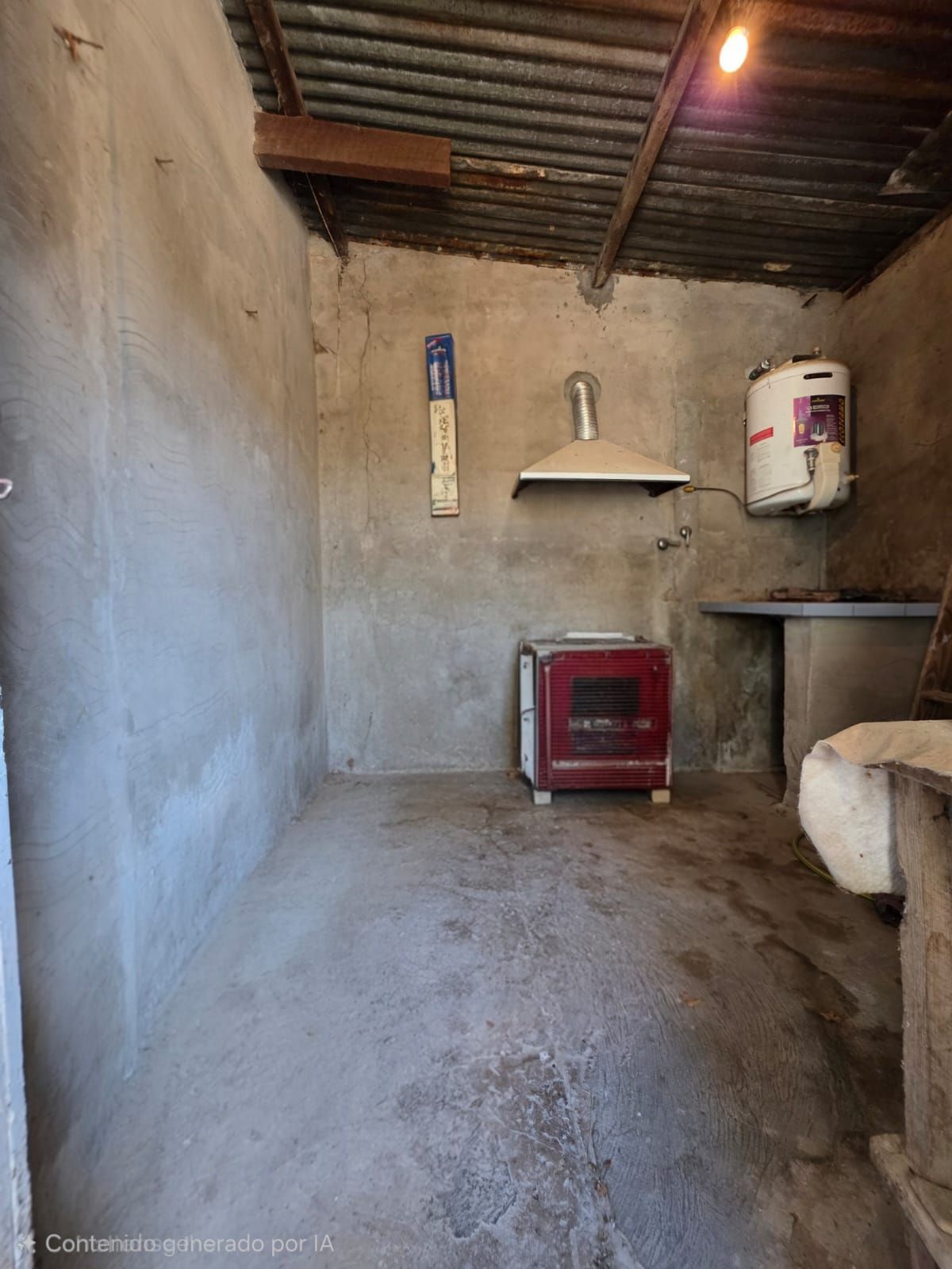 Pequeña habitación rústica con paredes de hormigón, techo de chapa ondulada, estufa roja y calentador de agua colgante.