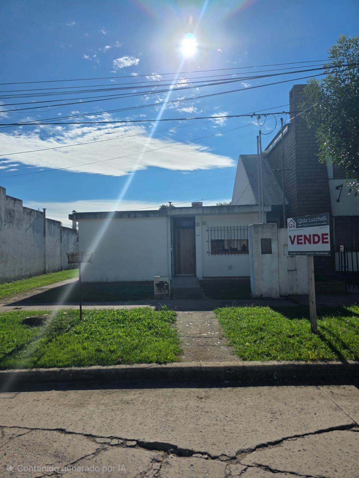 Pequeña casa blanca con un letrero de “Se vende”, jardín delantero y un cielo soleado y brillante.