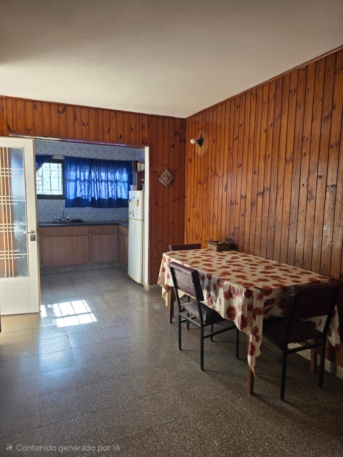 Pequeño comedor con paredes revestidas de madera, una mesa con mantel a cuadros y una cocina visible