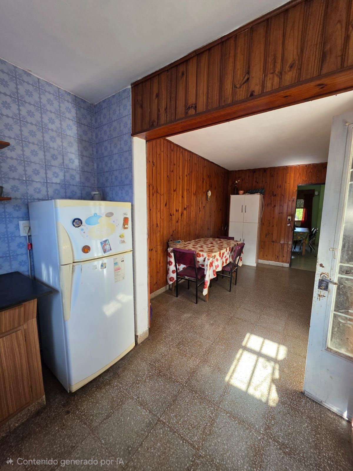 Cocina pequeña con refrigerador blanco, paredes revestidas de madera y una mesa en una habitación alicatada.