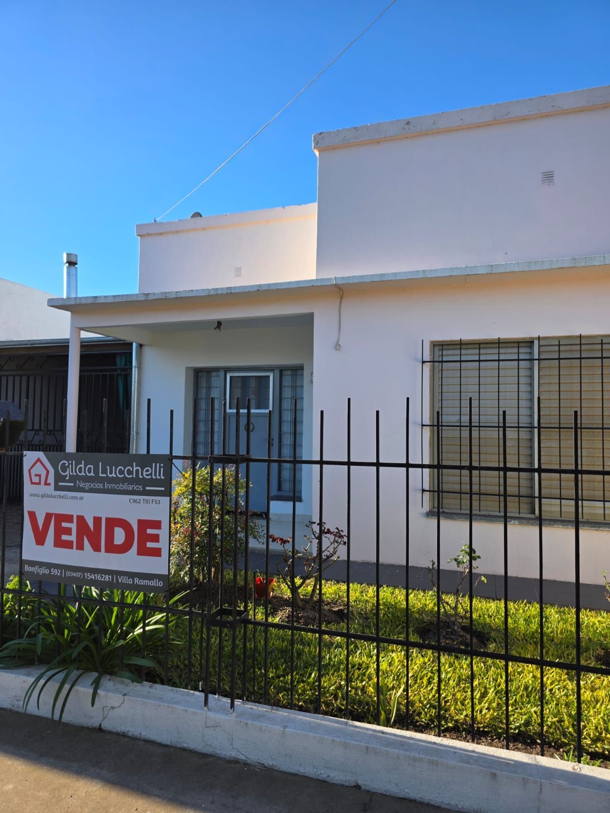Un cartel verde indica que se vende una casa pequeña de color verde menta al atardecer.