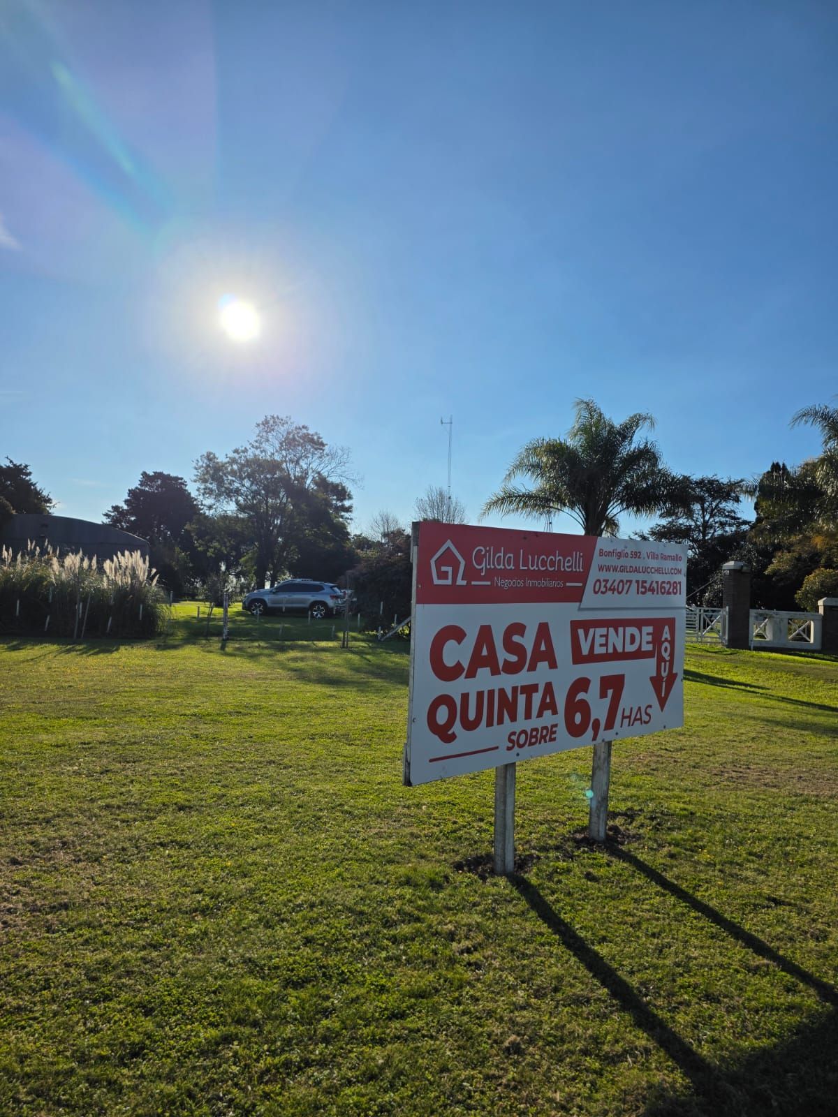 Pequeña casa blanca con un letrero de “Se vende”, jardín delantero y un cielo soleado y brillante.