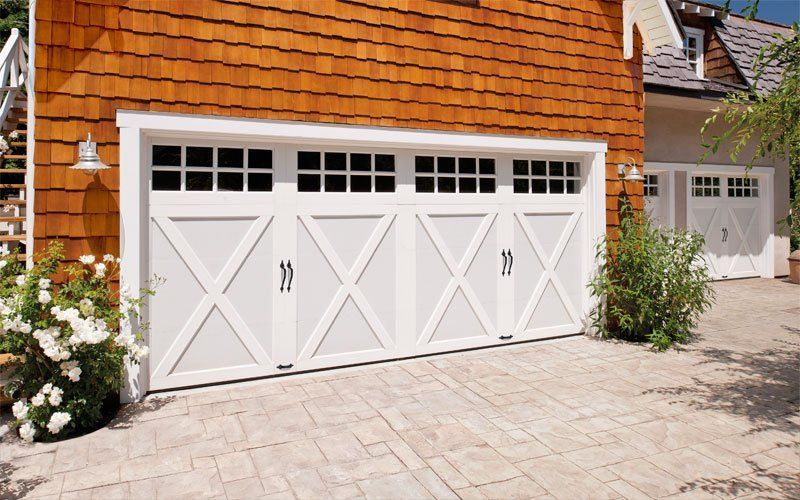 White carriage-style garage door with X-shaped accents and grid windows, next to brown wooden siding.