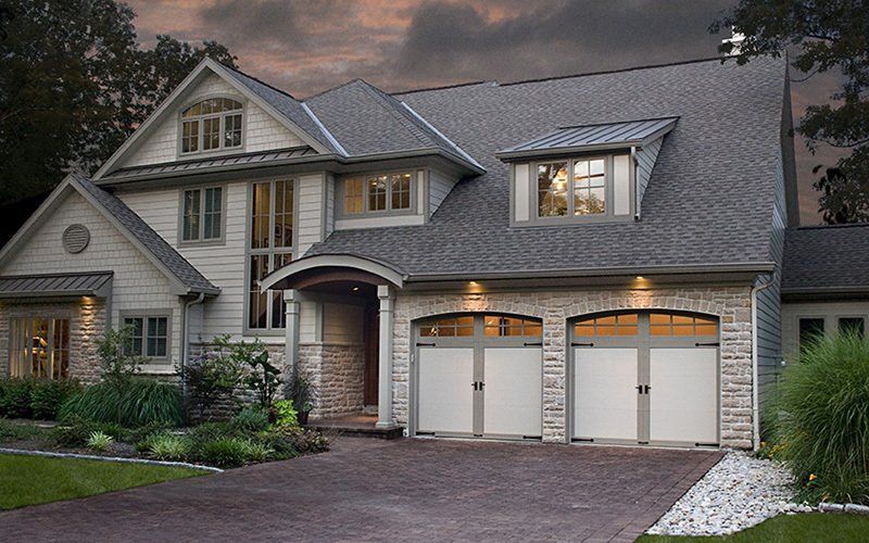 Two-story house with gray roof, stone facade, and two-car garage. Driveway with landscaping.