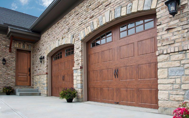 Brown garage doors with arched tops, stone facade, and a side door.
