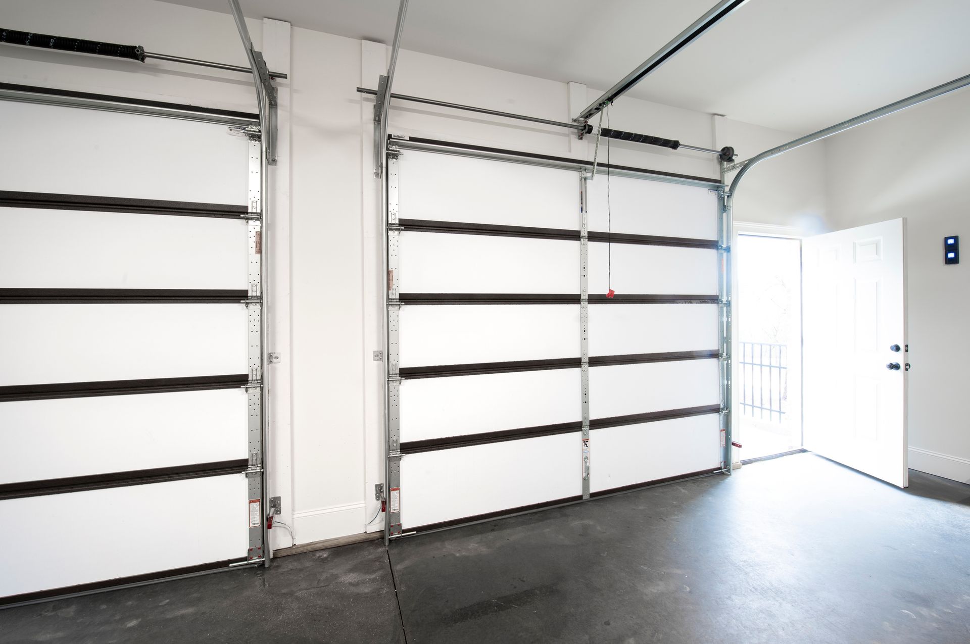 Interior view of a garage with two closed white garage doors, and a white open door on the right.