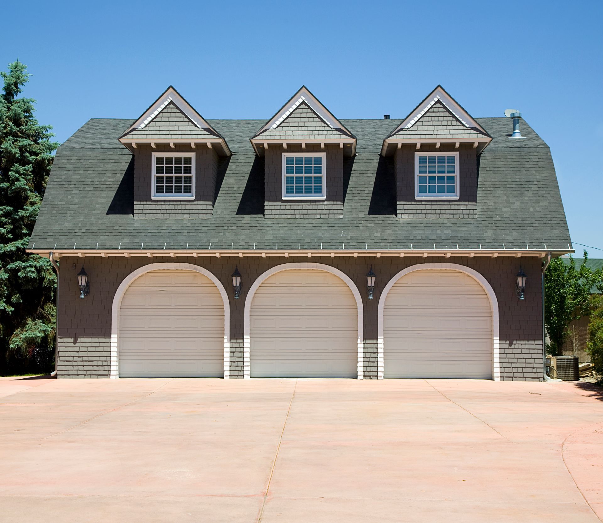 Three-car garage with arched doors, gray roof, and dormers under a blue sky.