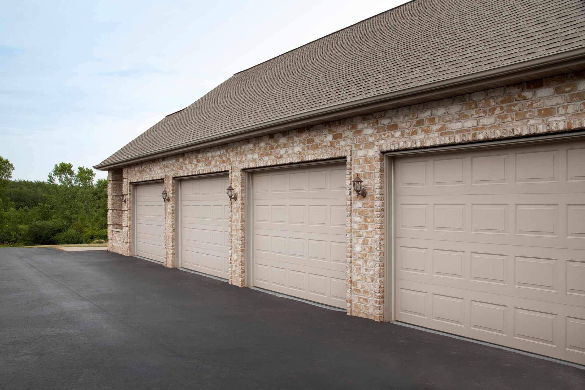 Three-car garage with tan doors and brick facade under a patterned brown roof, asphalt driveway.