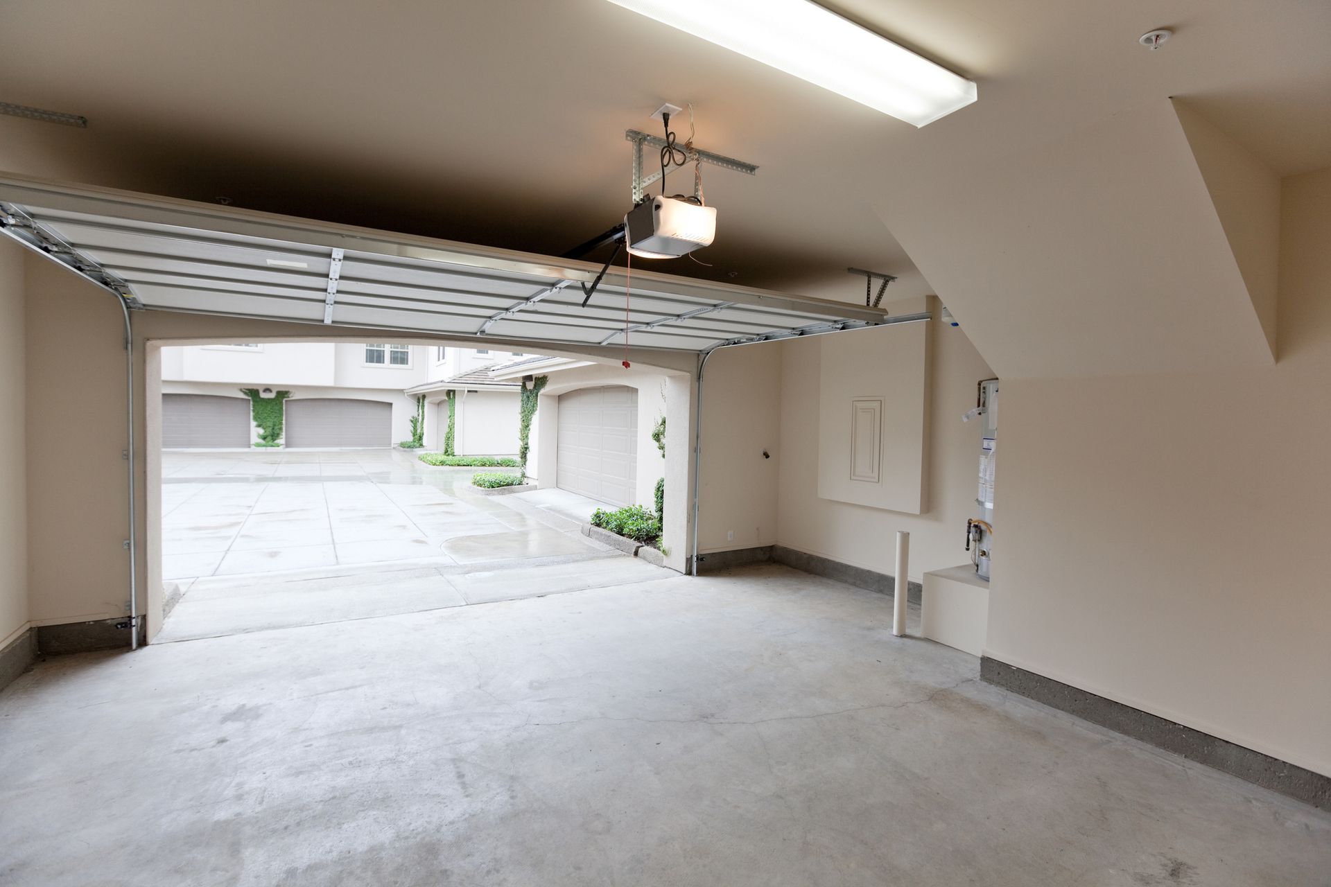 Empty garage with open door, leading to a driveway and other garages. Concrete floor, white walls.