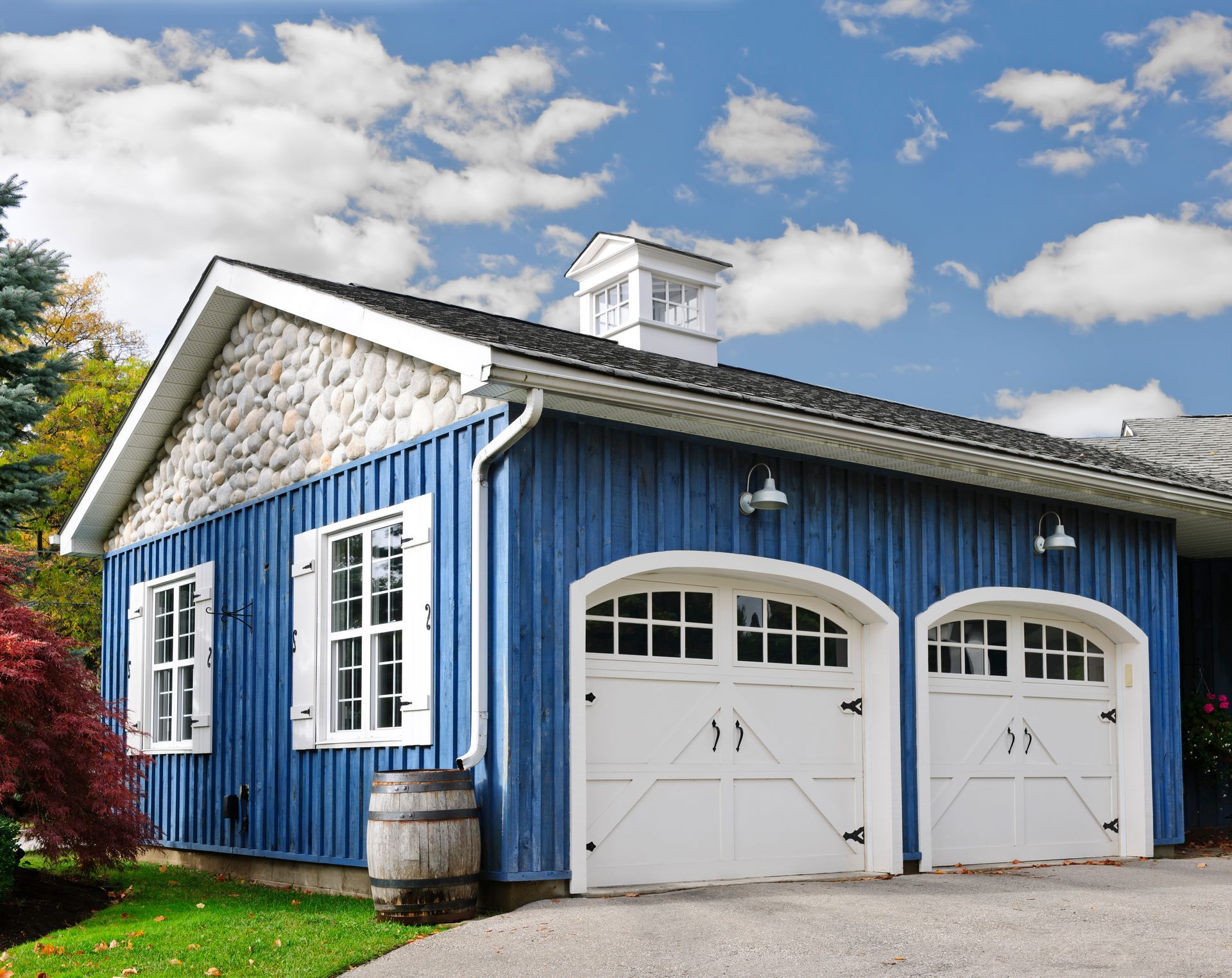 Blue garage with white doors and stone facade under cloudy sky.