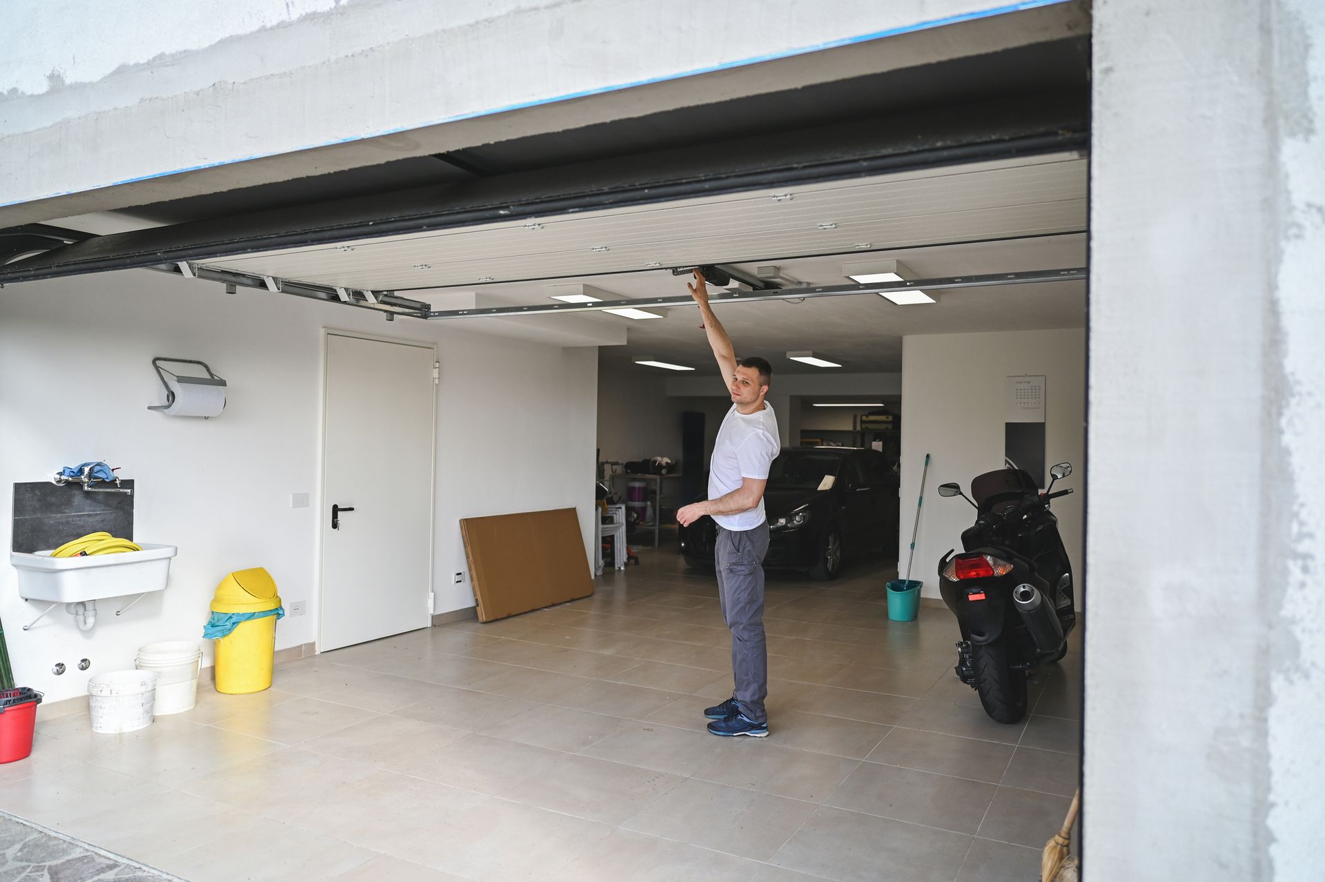 Man inside garage, reaching up toward the ceiling. Garage contains a motorcycle and other items.