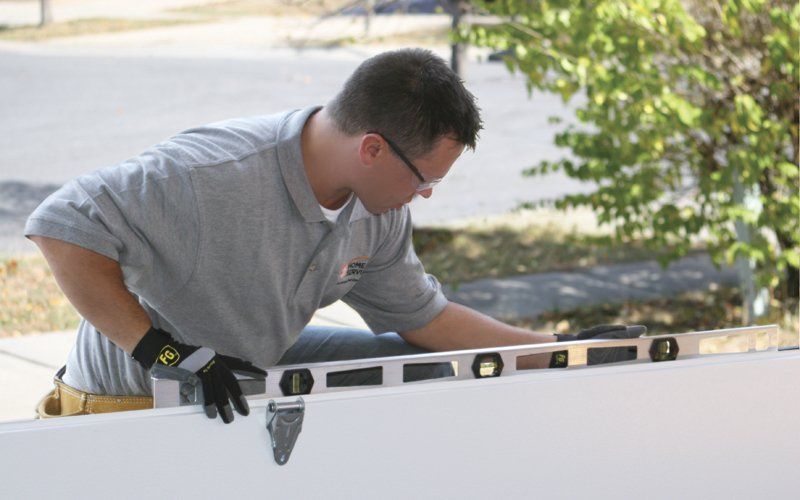 Man in gray shirt uses a level on a white surface outdoors.
