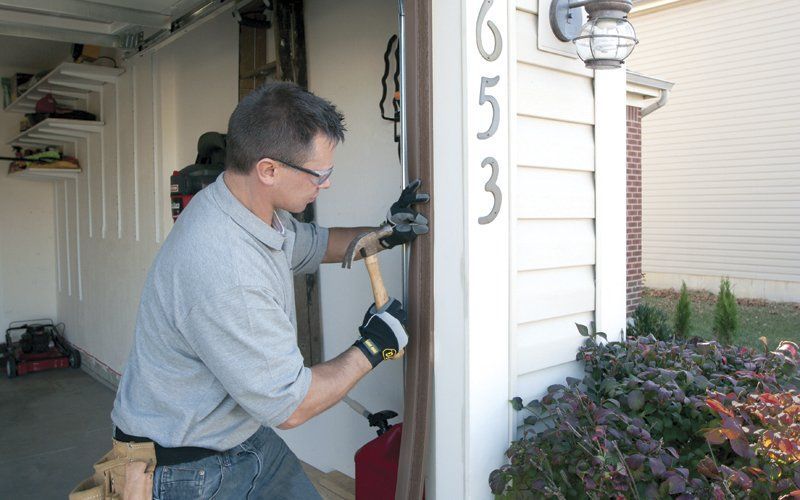 Man hammers trim on a house near the garage.