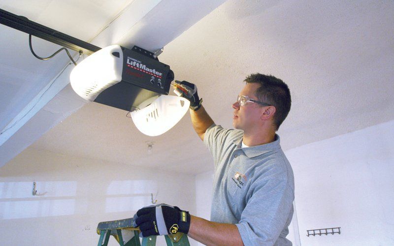 Man on ladder installs a garage door opener in a garage.