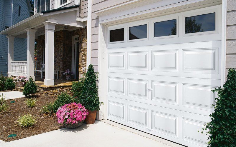 White garage door on a house with a porch and landscaping.