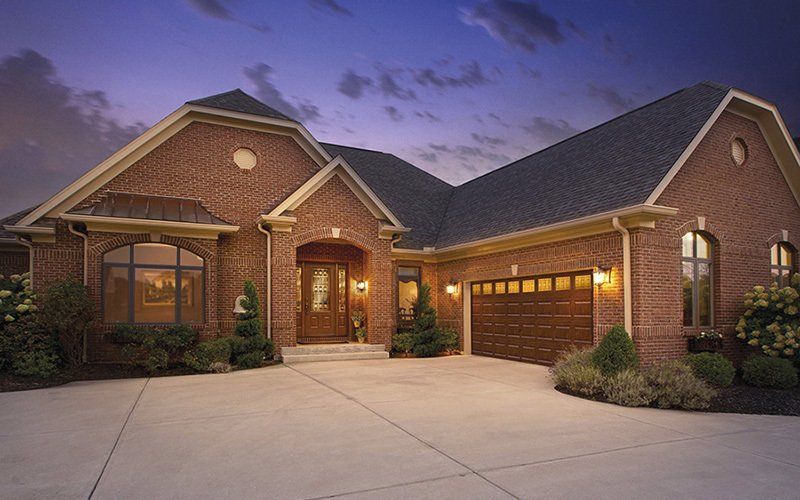 Brick house with dark roof and garage, driveway, and landscaping.