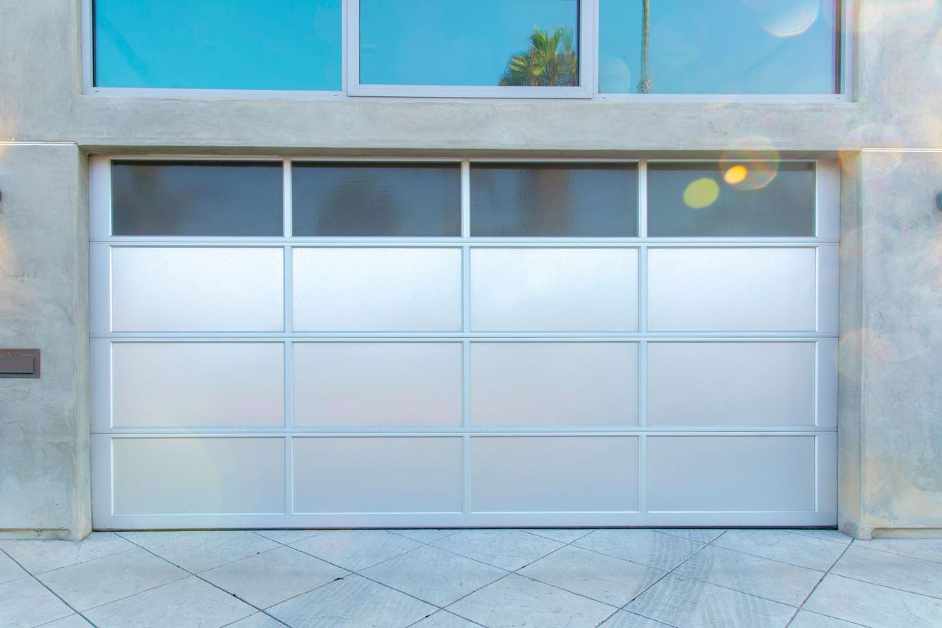 Modern, silver garage door with frosted glass panels, built into a concrete facade.