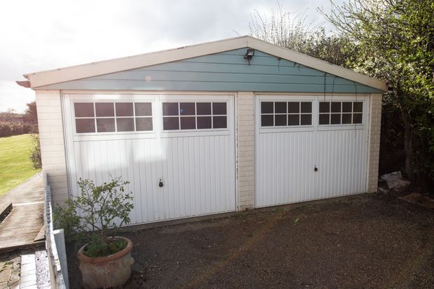 Double garage with white doors, blue trim, and gravel driveway.