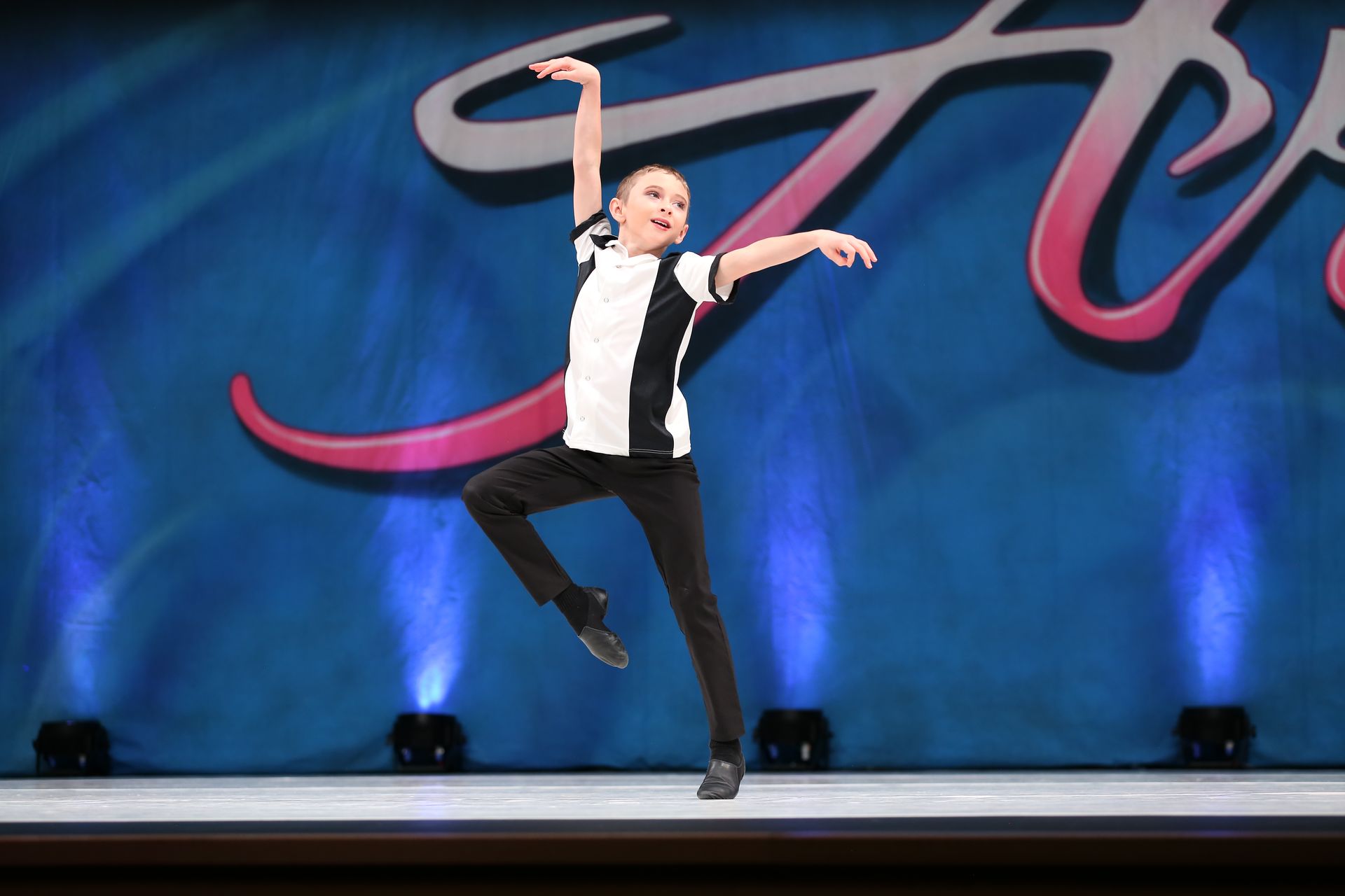 A person in a black and white top and black pants performs a dance move on a stage with a blue, lit background. E-Street Dance Academy, Edgewood, MD