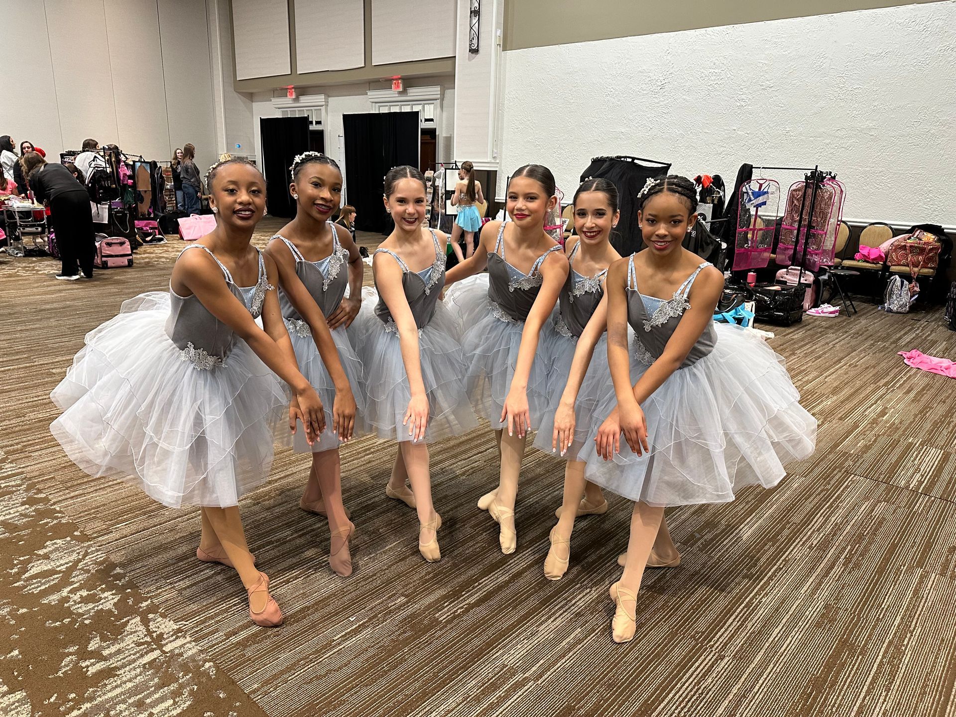 Six dancers in matching silver tutus pose in a line on a carpeted floor in a large event space. E-Street Dance Academy, Edgewood, MD