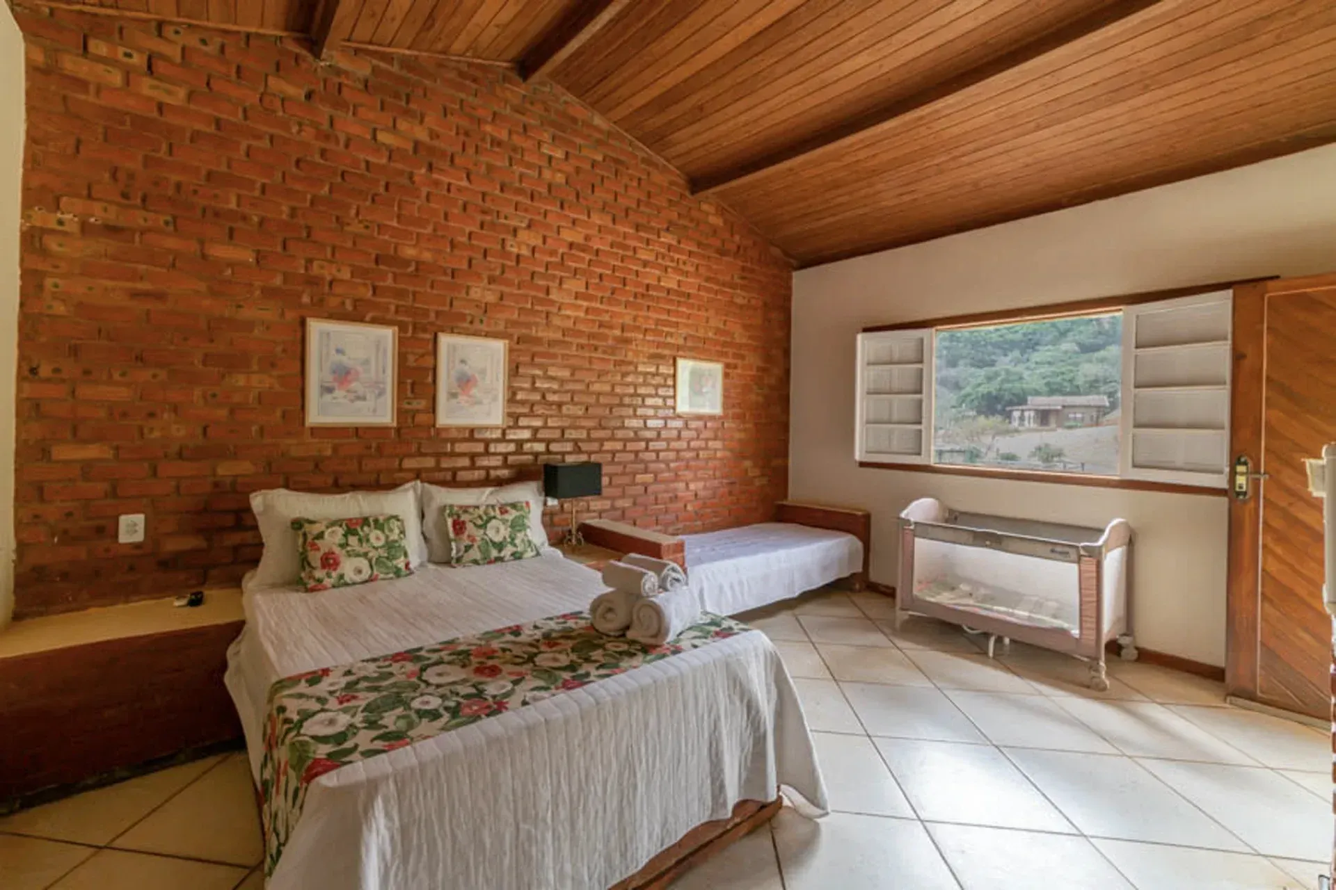 Um quarto com parede de tijolos, uma cama, um berço e uma janela.