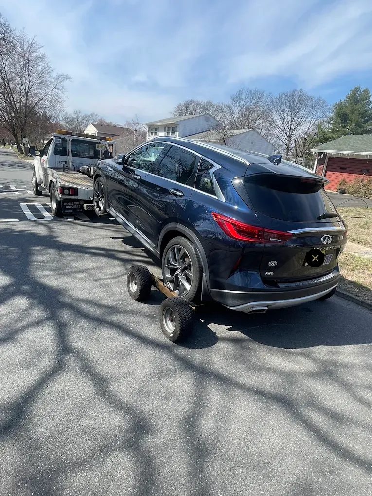 Dark blue SUV being towed on a dolly by a tow truck on a sunny street.